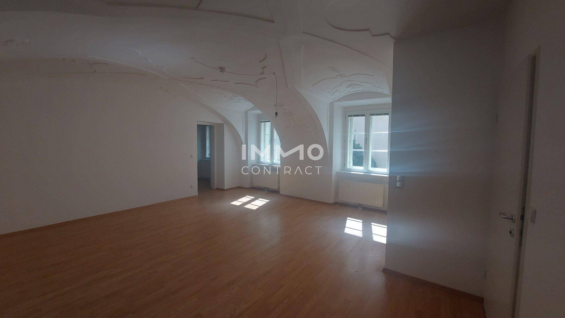 Helles Wohnzimmer mit elegantem Holzboden und kunstvoll verzierter Gewölbedecke, durchflutet von Tageslicht.