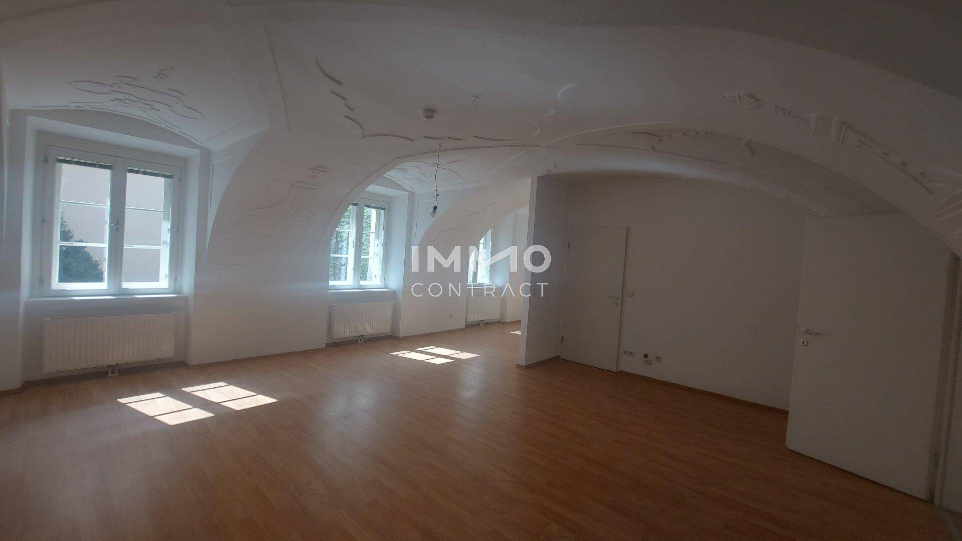 Lichtdurchfluteter Wohnraum mit Holzboden, zwei großen Fenstern und einer prächtigen Gewölbedecke.