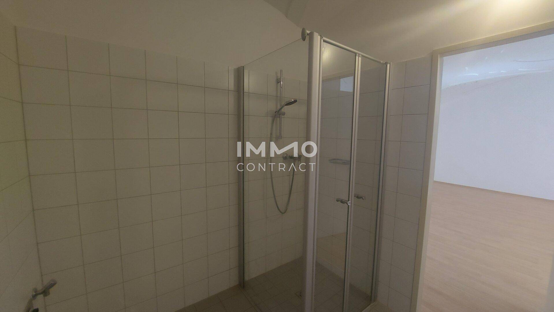 Badezimmer mit hellen Fliesen und einer modernen Duschkabine aus Glas.