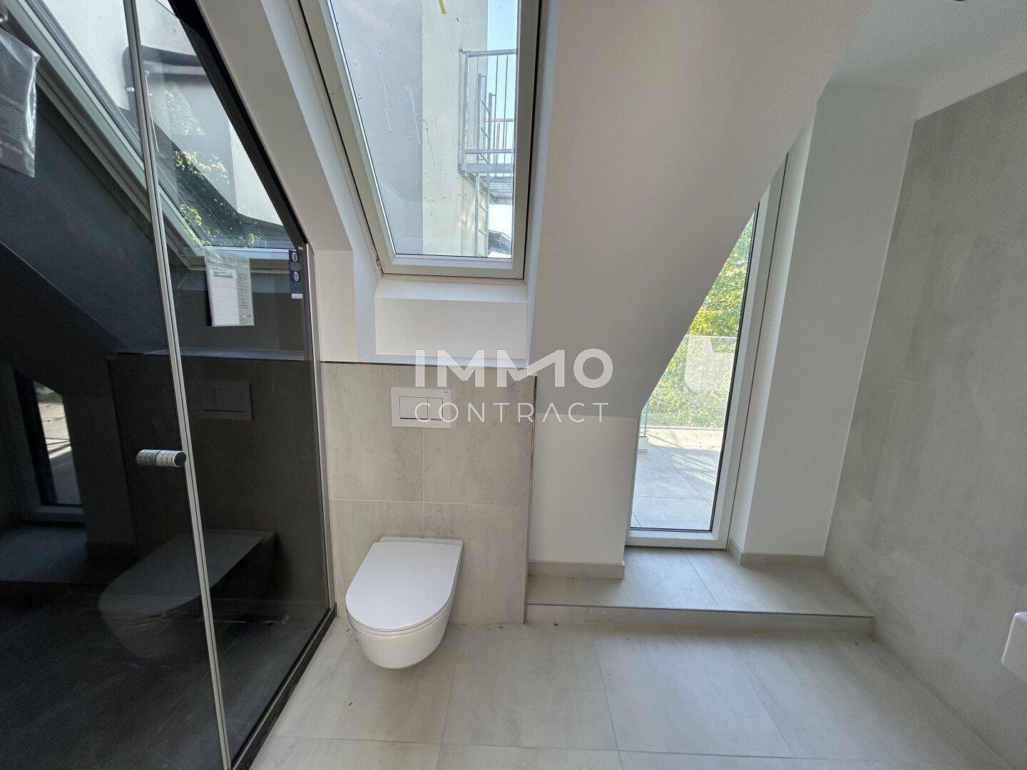 Modernes Badezimmer mit wandhängendem WC, Duschkabine und Dachfenster für Tageslicht.