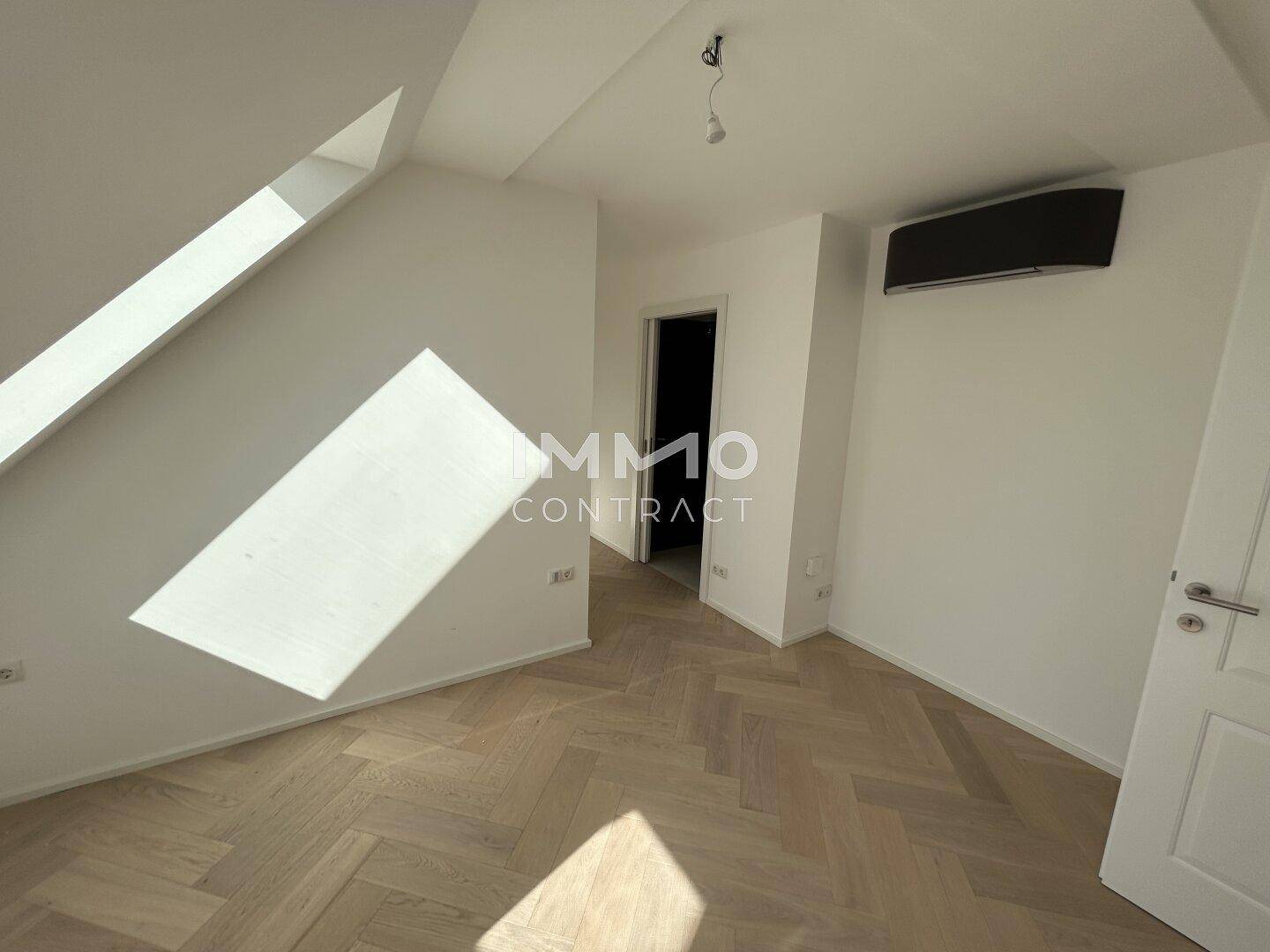 Helles Schlafzimmer im Dachgeschoss mit Parkettboden, Dachfenster und Klimaanlage.