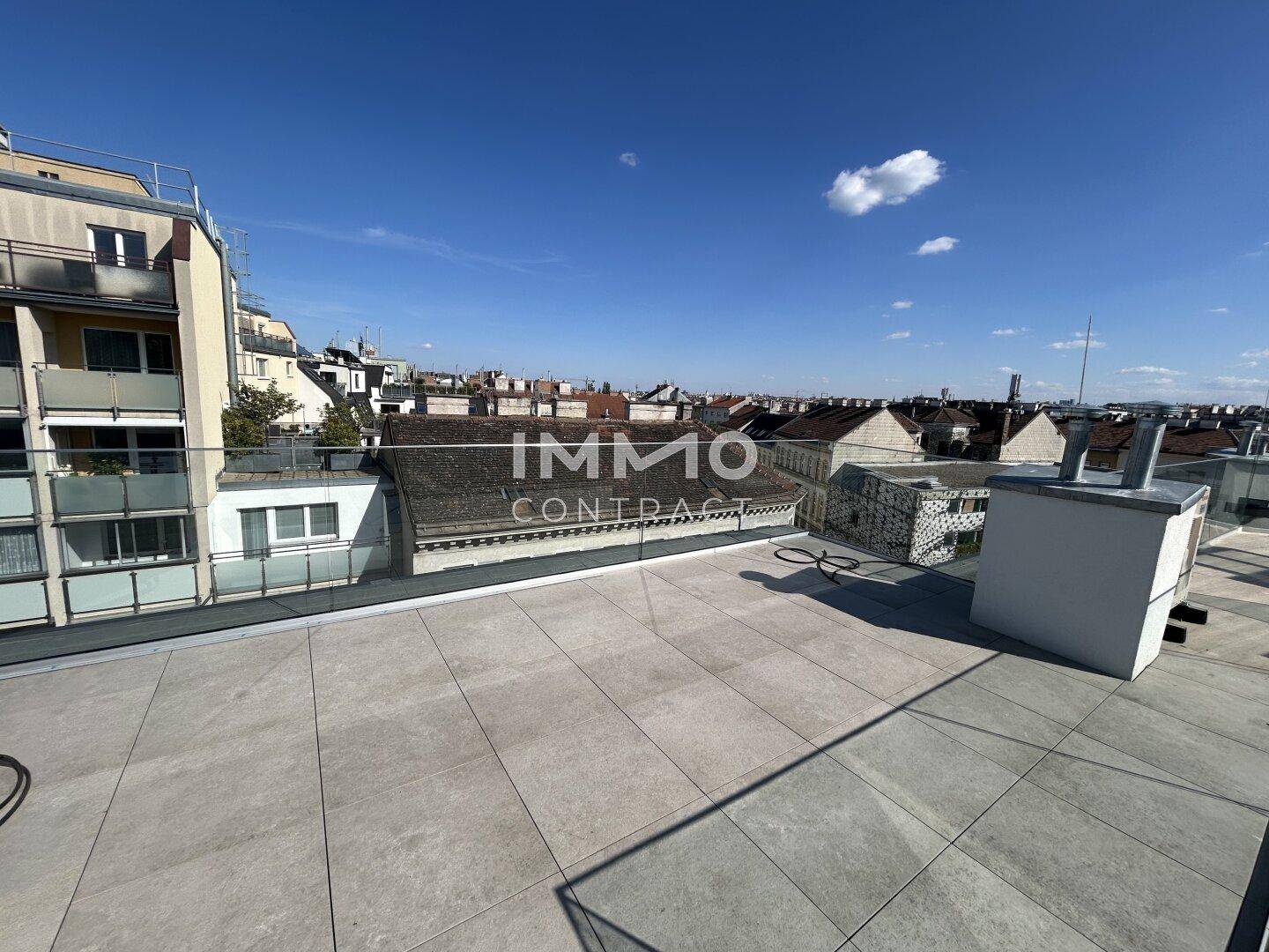 Weitläufige Dachterrasse mit Fliesenboden und Blick über die Dächer der Stadt.