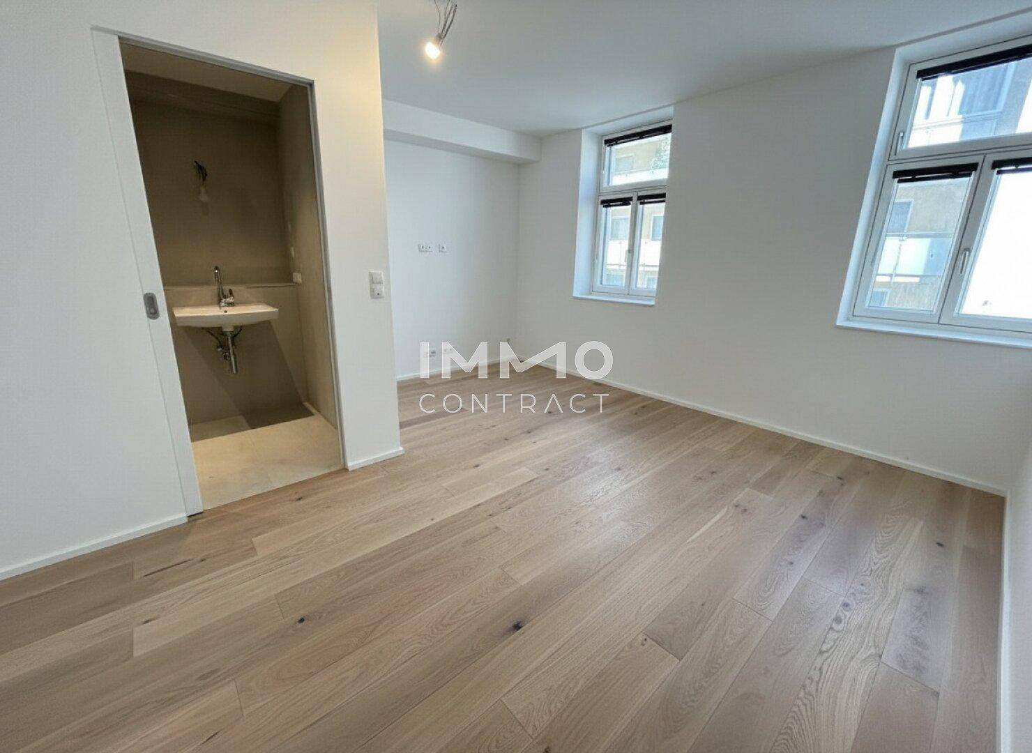 Geräumiges Zimmer mit hellem Parkettboden und Zugang zu einem Badezimmer oder WC.