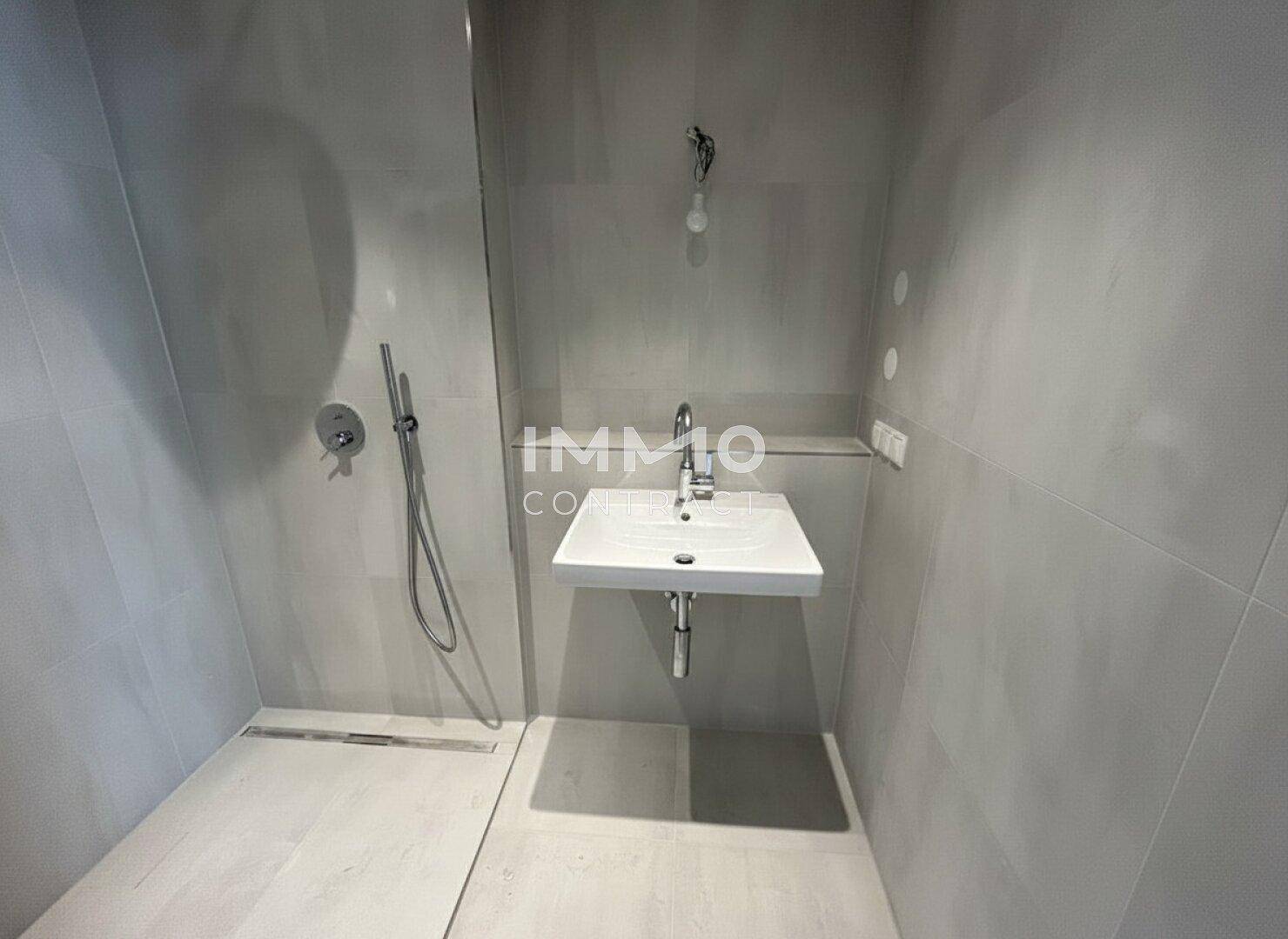 Modernes Badezimmer mit ebenerdiger Dusche, Waschbecken und grauen Fliesen.
