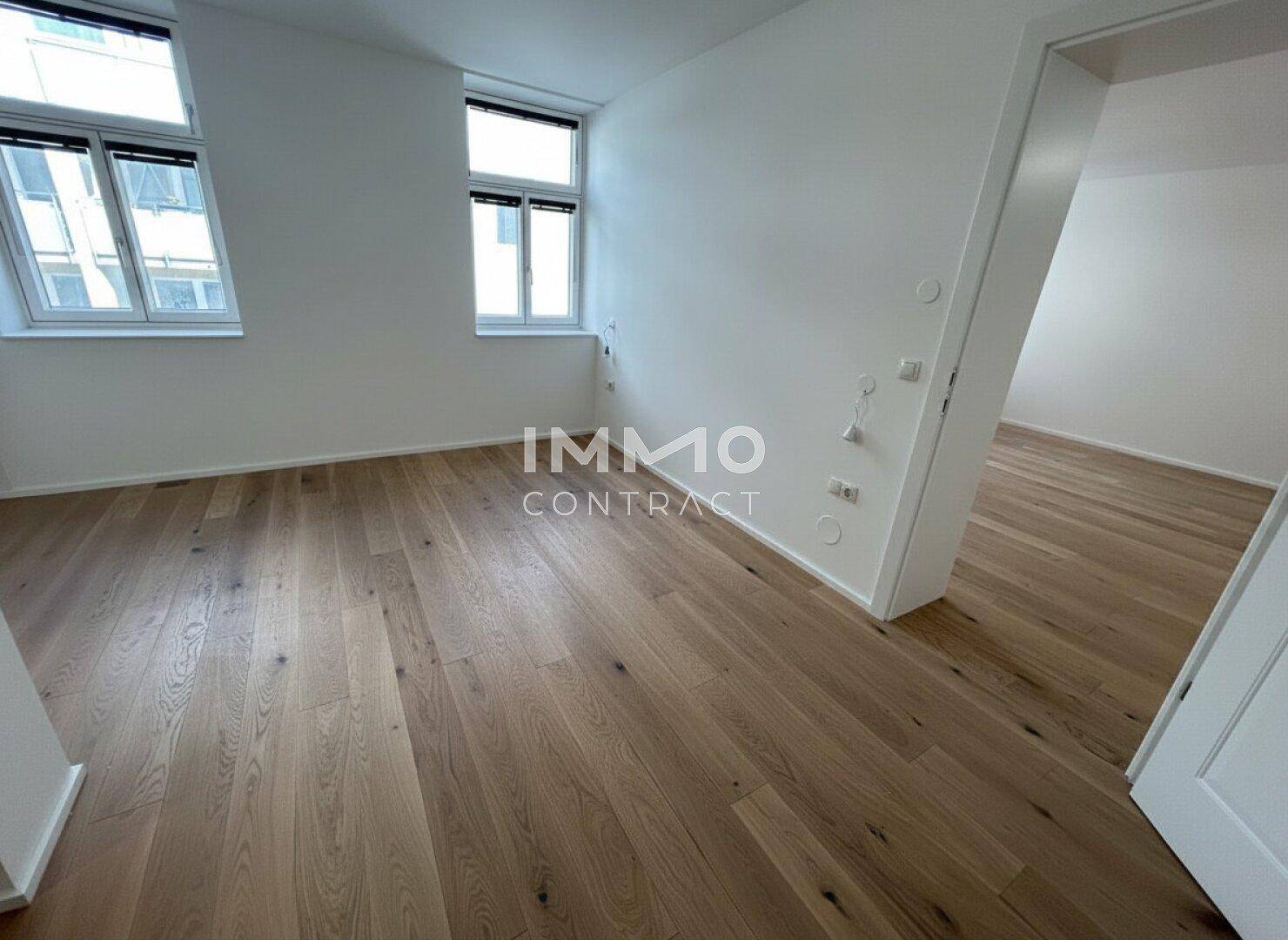 Lichtdurchfluteter Raum mit Holzparkett und Zugang zu einem weiteren Zimmer.