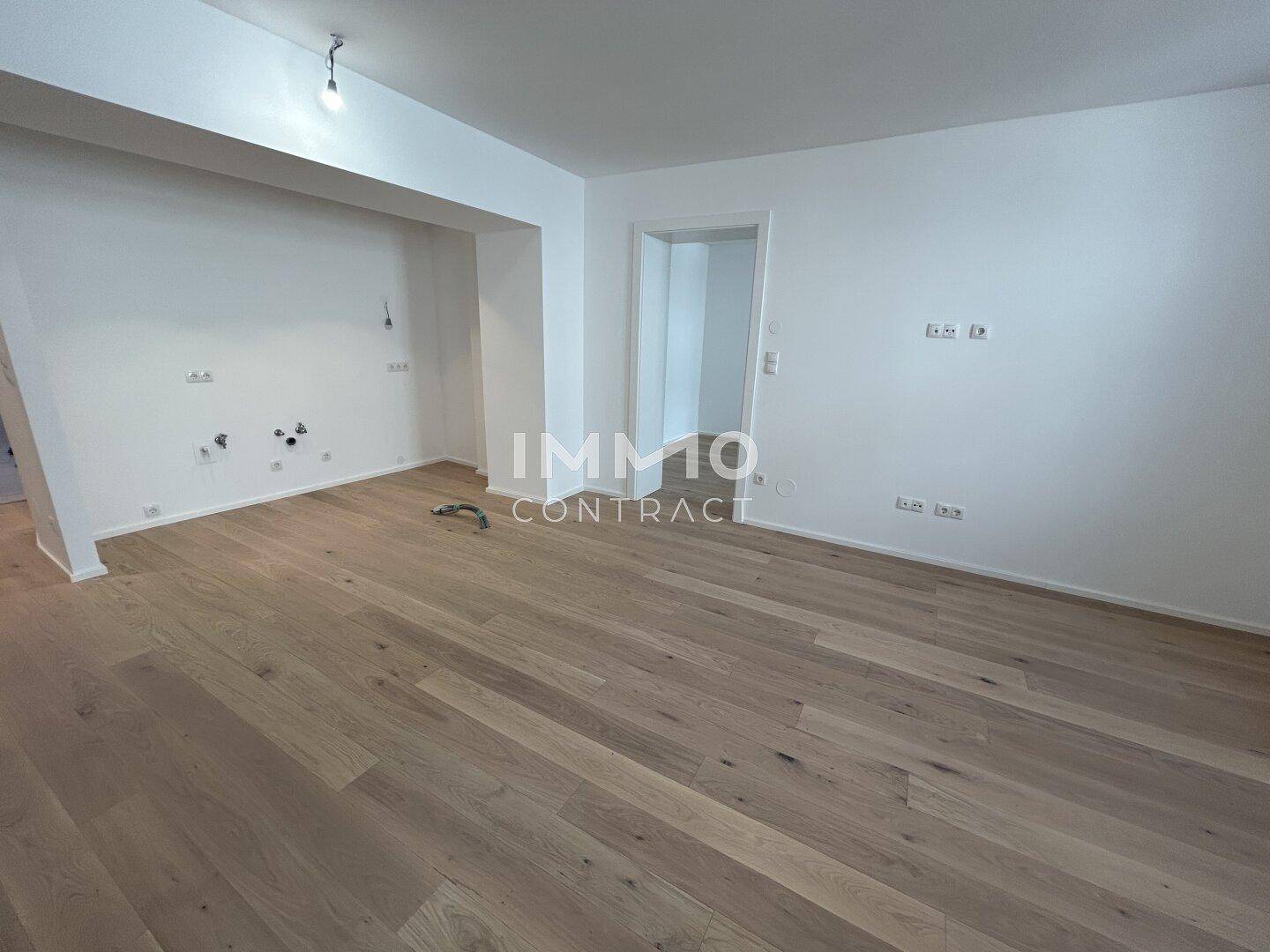 Heller Raum mit Anschlüssen für eine Küche und neuem Holzparkettboden.