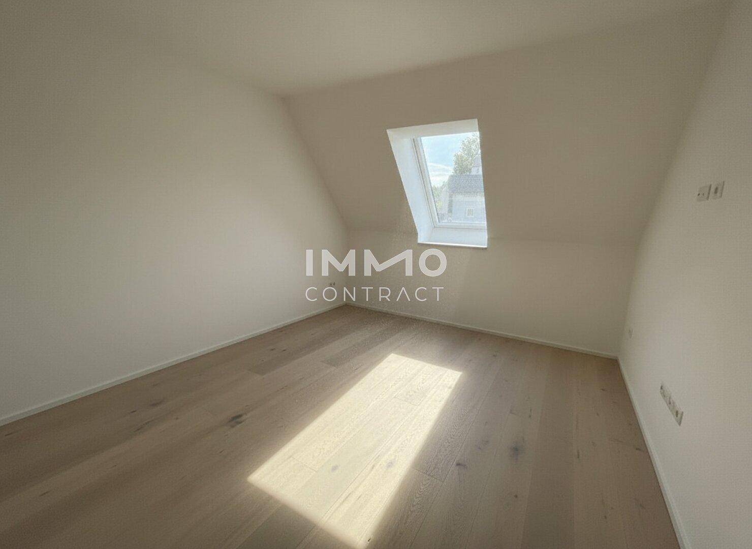 Leeres Zimmer im Dachgeschoss mit hellem Holzboden und einem Dachfenster.