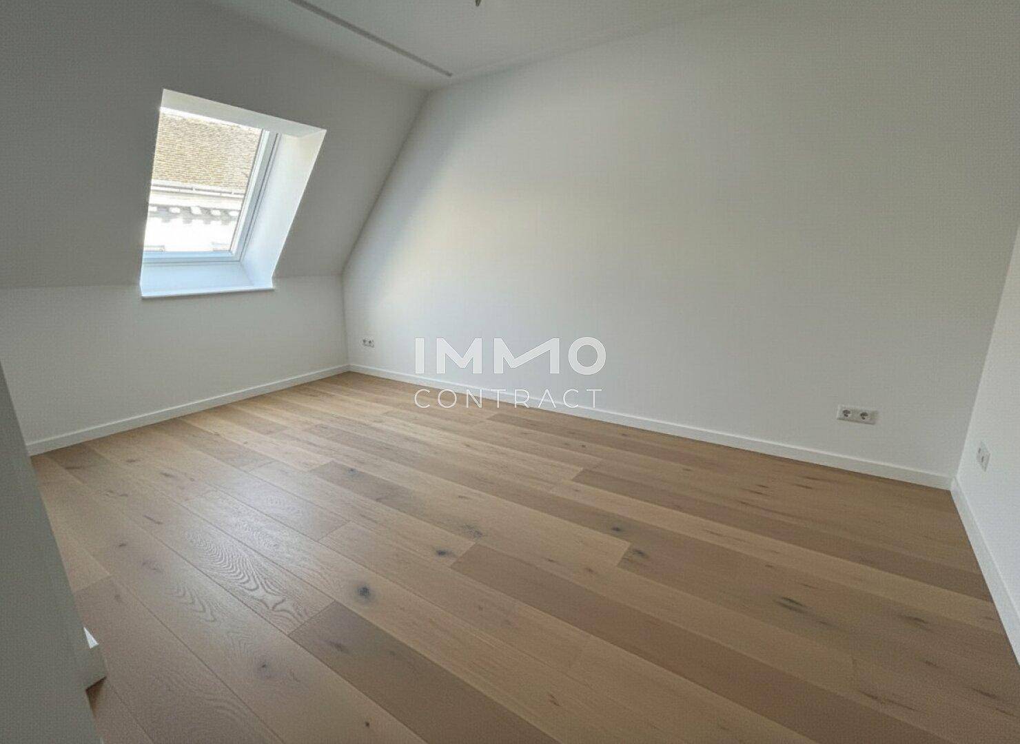 Geräumiges, leeres Zimmer mit Holzboden und einem Dachfenster, ideal als Schlafzimmer.