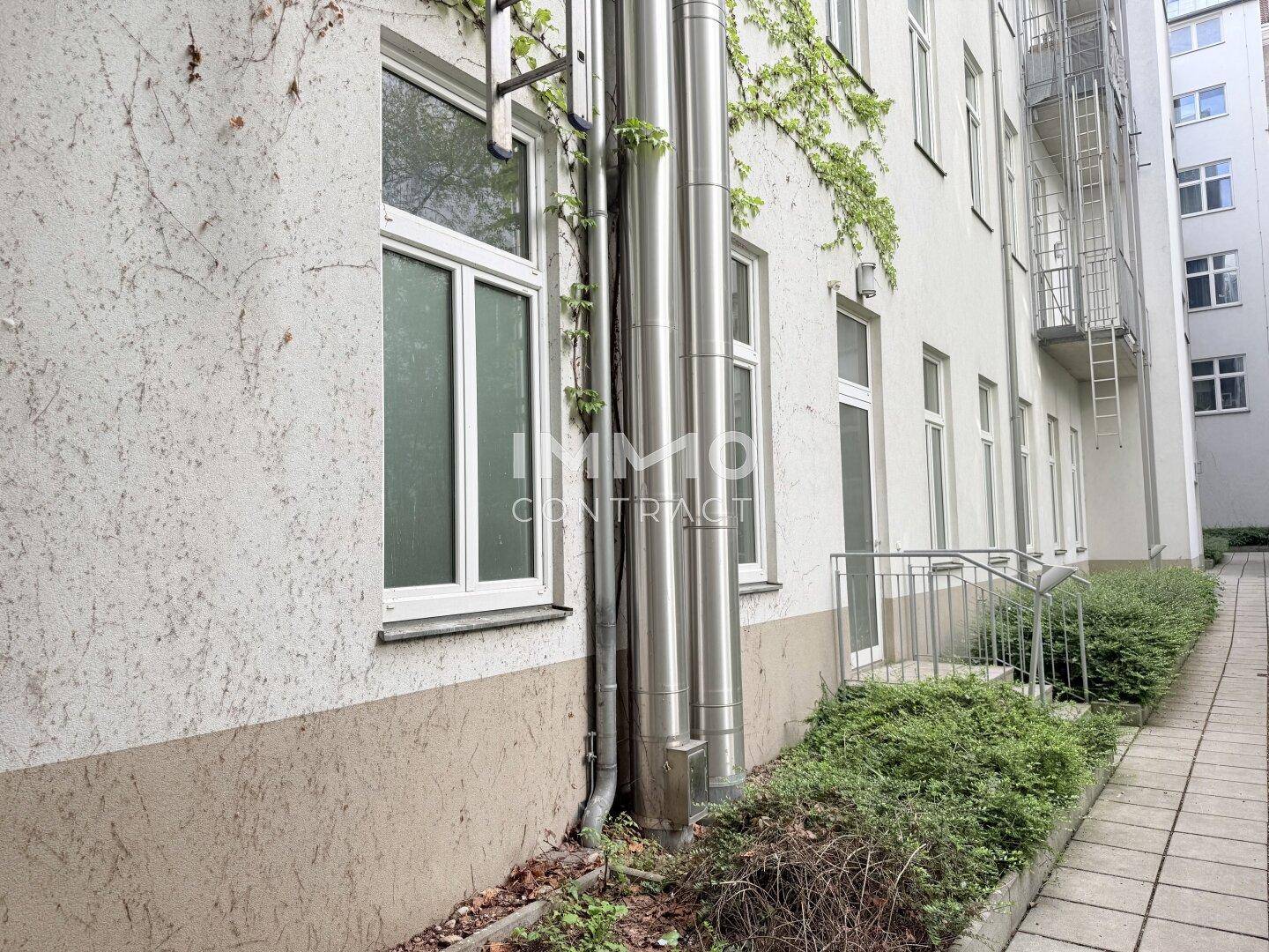 Seitenansicht eines Gebäudes mit Fenstern, Fallrohren und Kletterpflanzen an der Fassade, die eine natürliche Note verleihen.