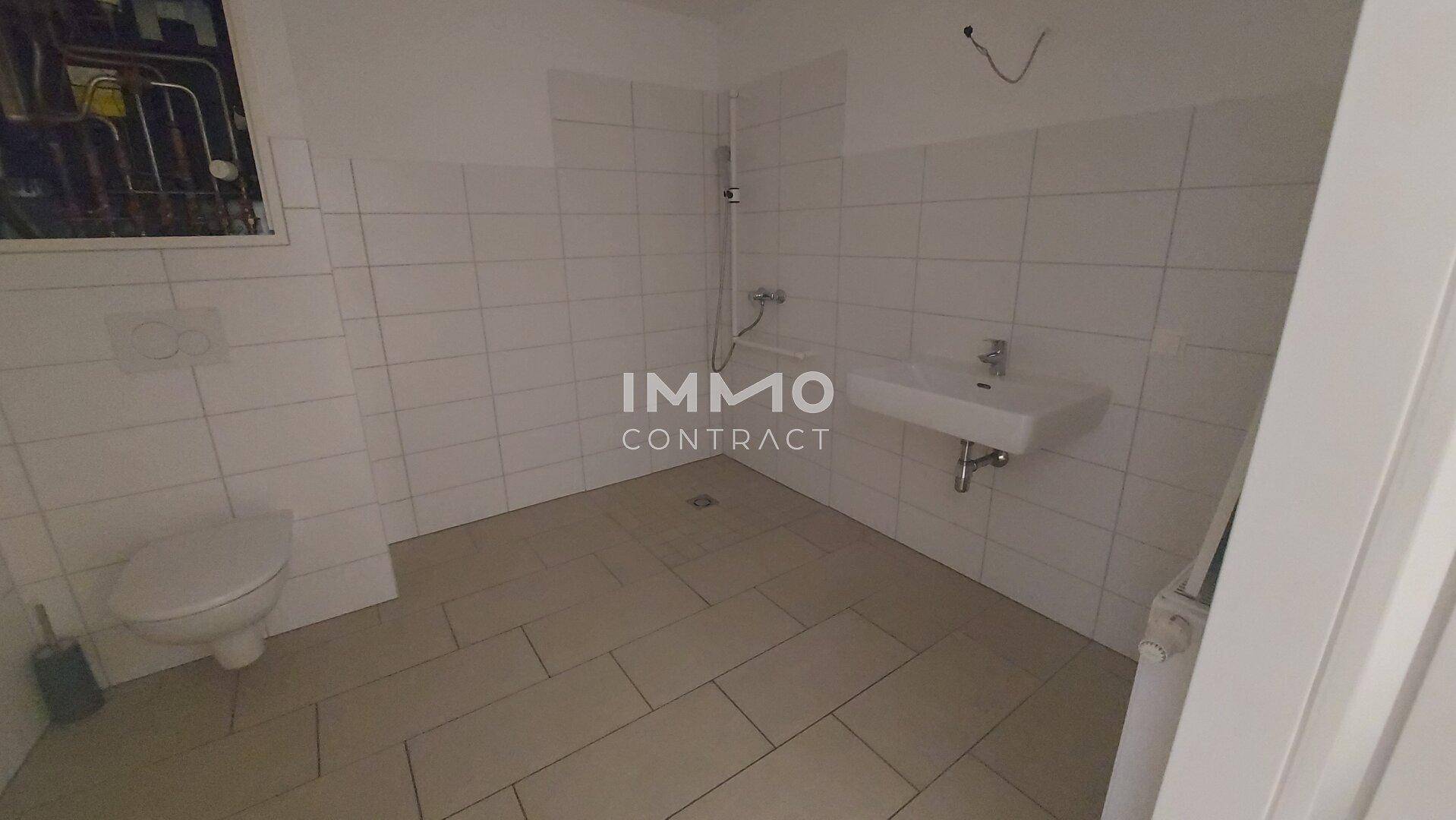 Einfaches Badezimmer mit WC, Waschbecken und Dusche, gefliest mit hellen Fliesen.