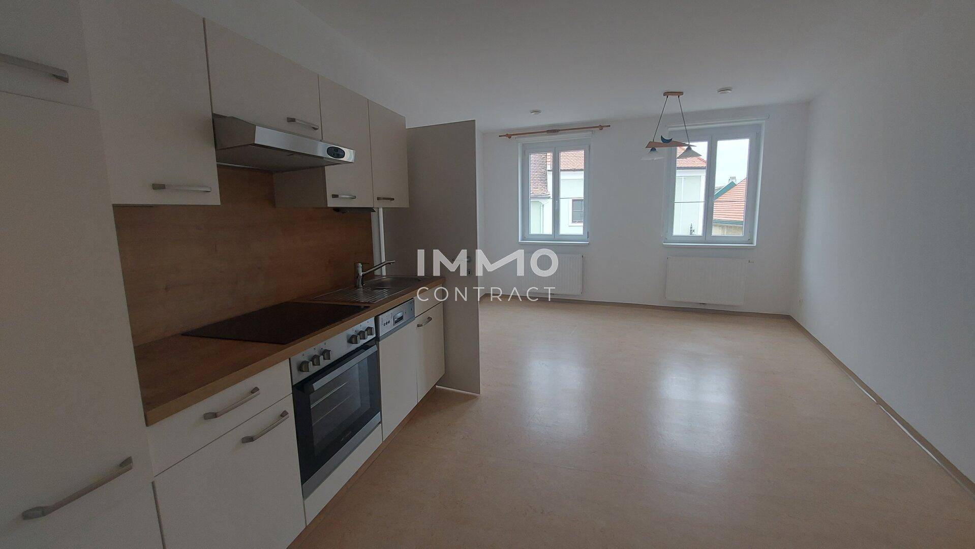 Offener Wohnbereich mit integrierter Küche, Laminatboden und zwei großen Fenstern.