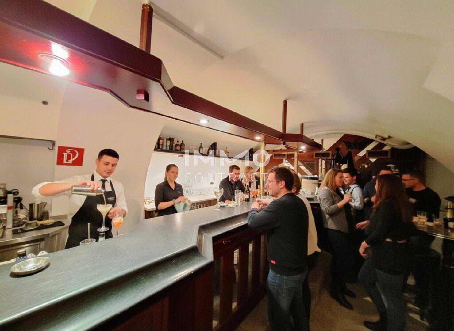 Barkeeper bereitet Cocktails an einer langen Holztheke zu, während Gäste die Atmosphäre genießen.