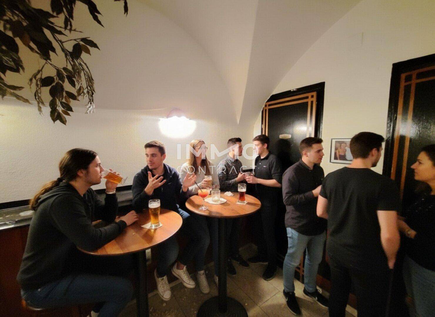 Gemütlicher Barbereich mit kleinen runden Tischen und Gästen, die sich unterhalten.