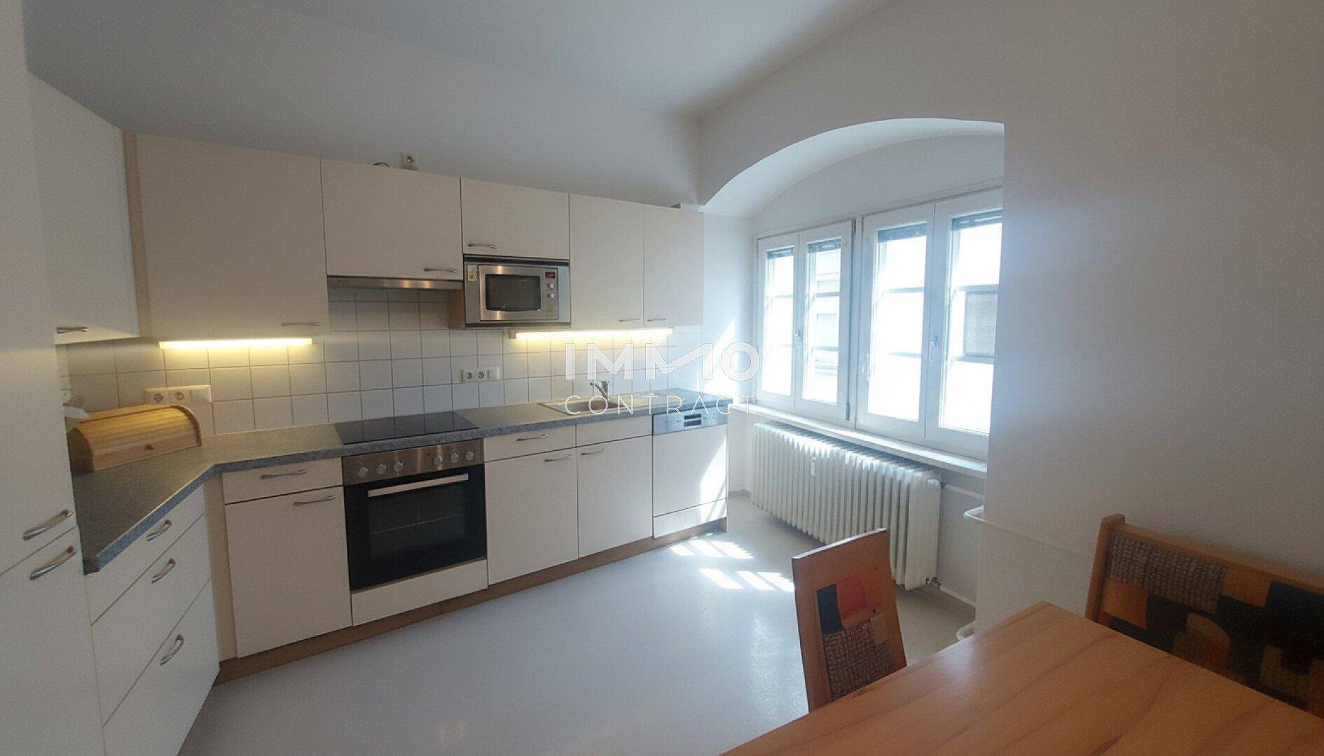 Helle Küche mit weißen Schränken, Fliesenrückwand und großem Fenster.