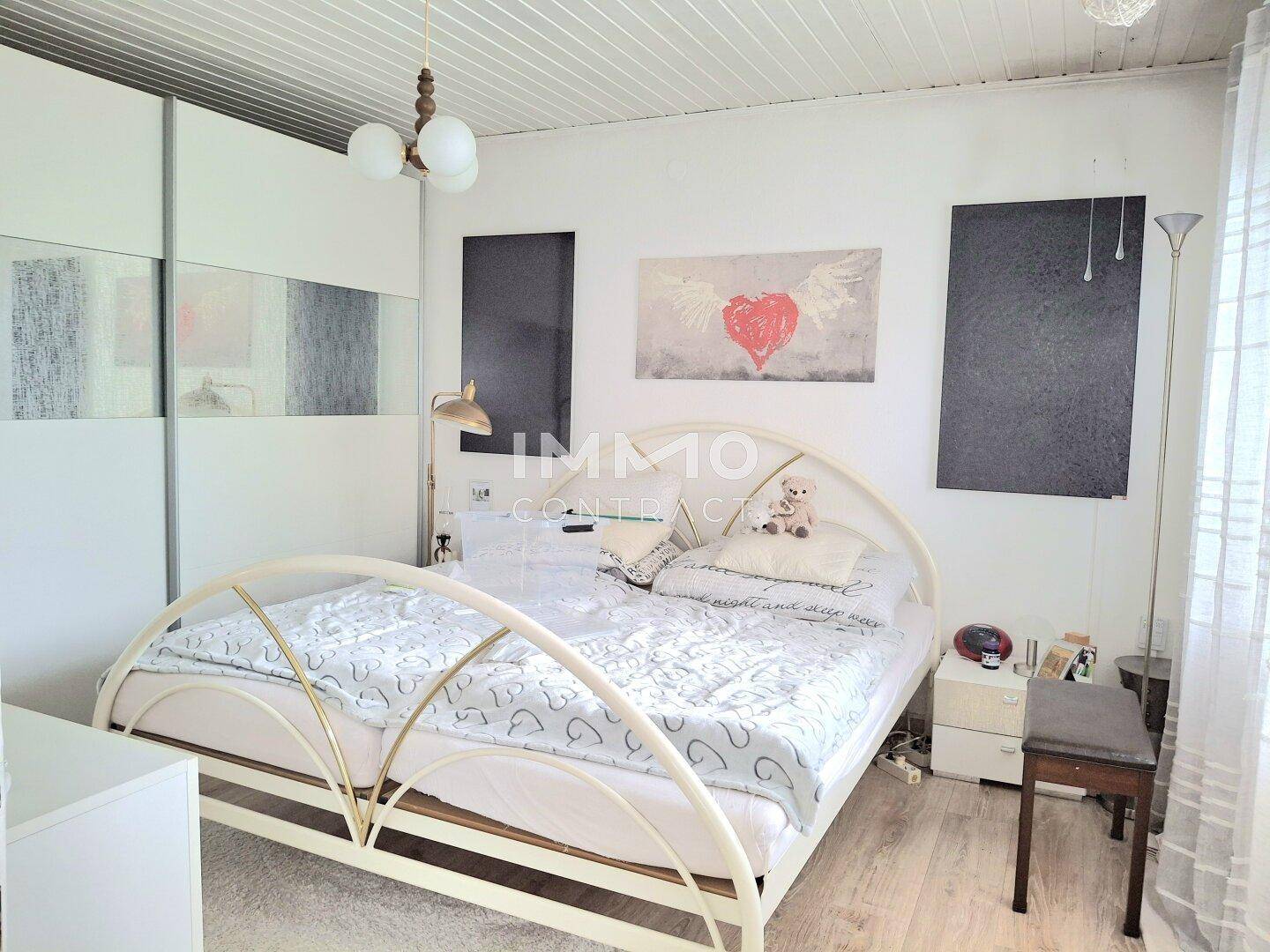 Schlafzimmer mit hellem Boden, weißem Metallbett und Schiebetürenschrank.