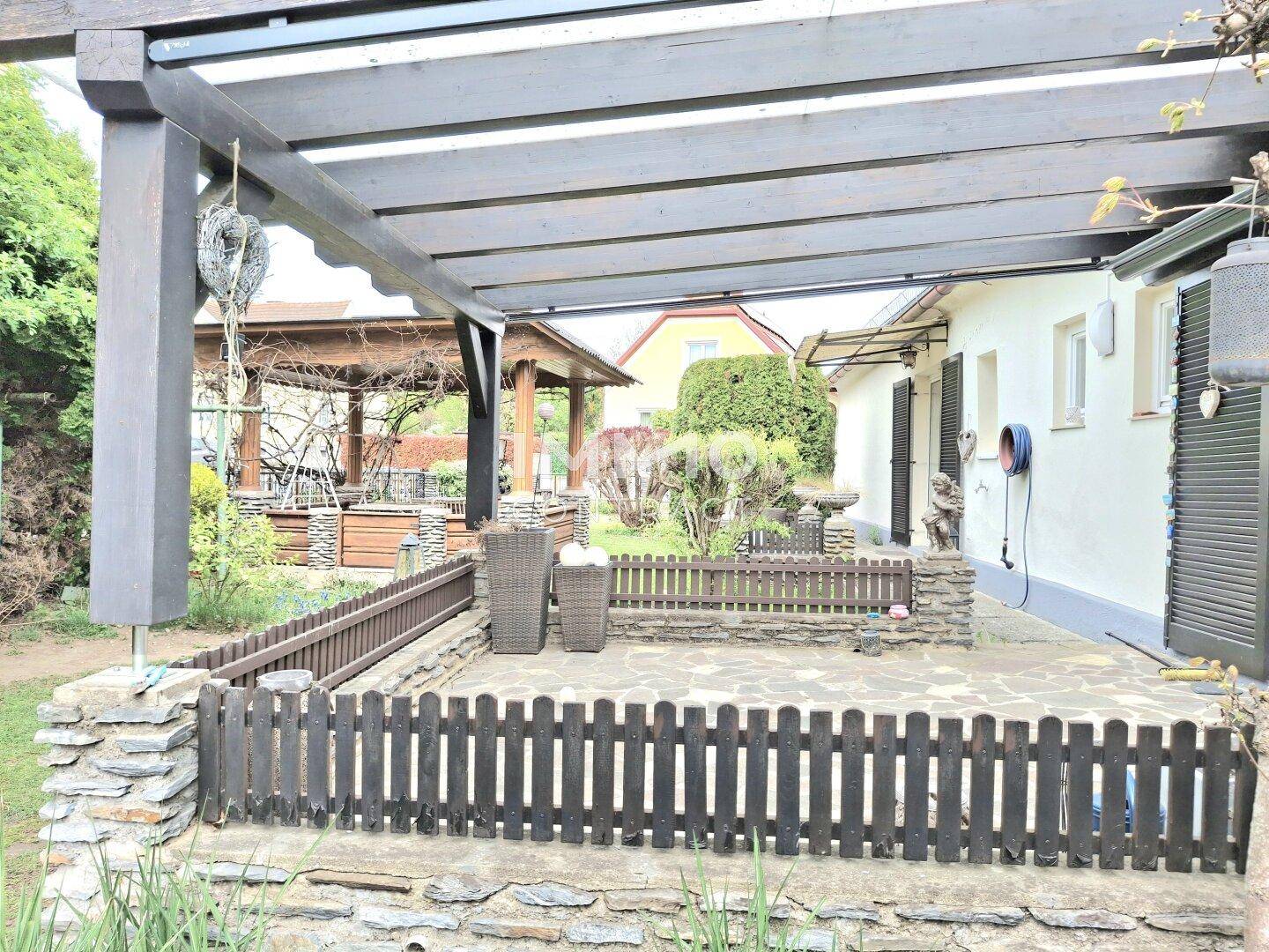 Geräumige Terrasse mit Pergola und Blick auf den Garten sowie das Hauptgebäude.