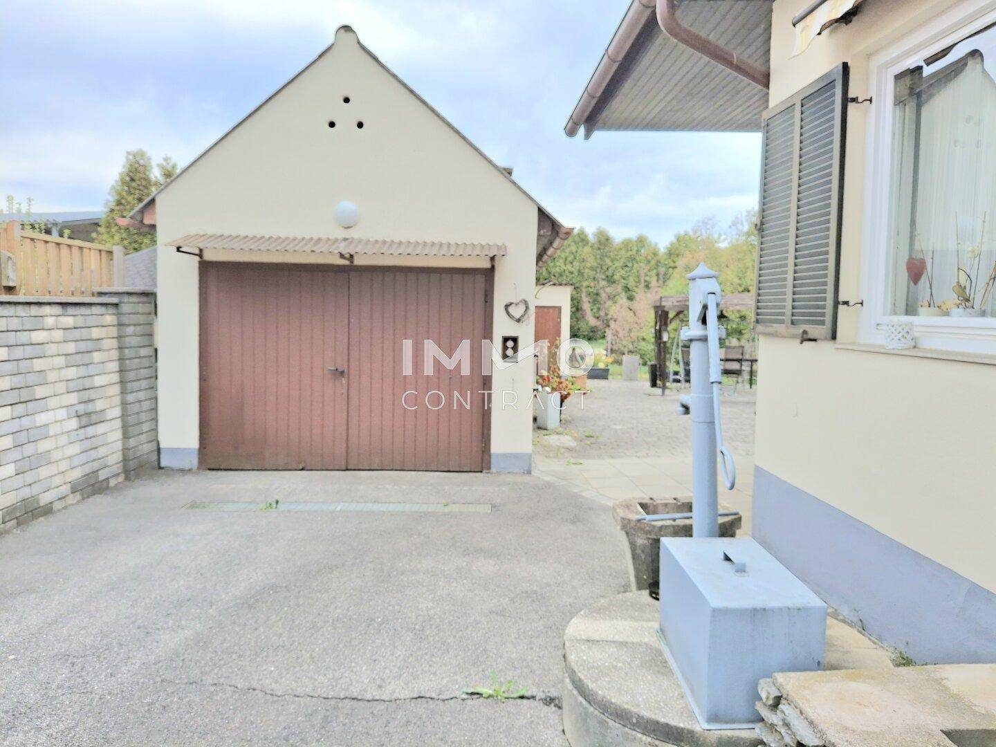 Freistehende Garage mit Holztor und einer traditionellen Wasserpumpe im Hofbereich.
