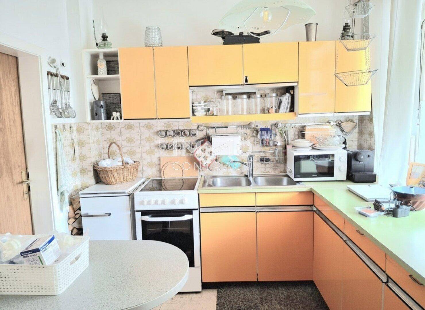 Funktionale Küche mit orangefarbenen Schränken, Doppelspüle und traditionellen Fliesen.