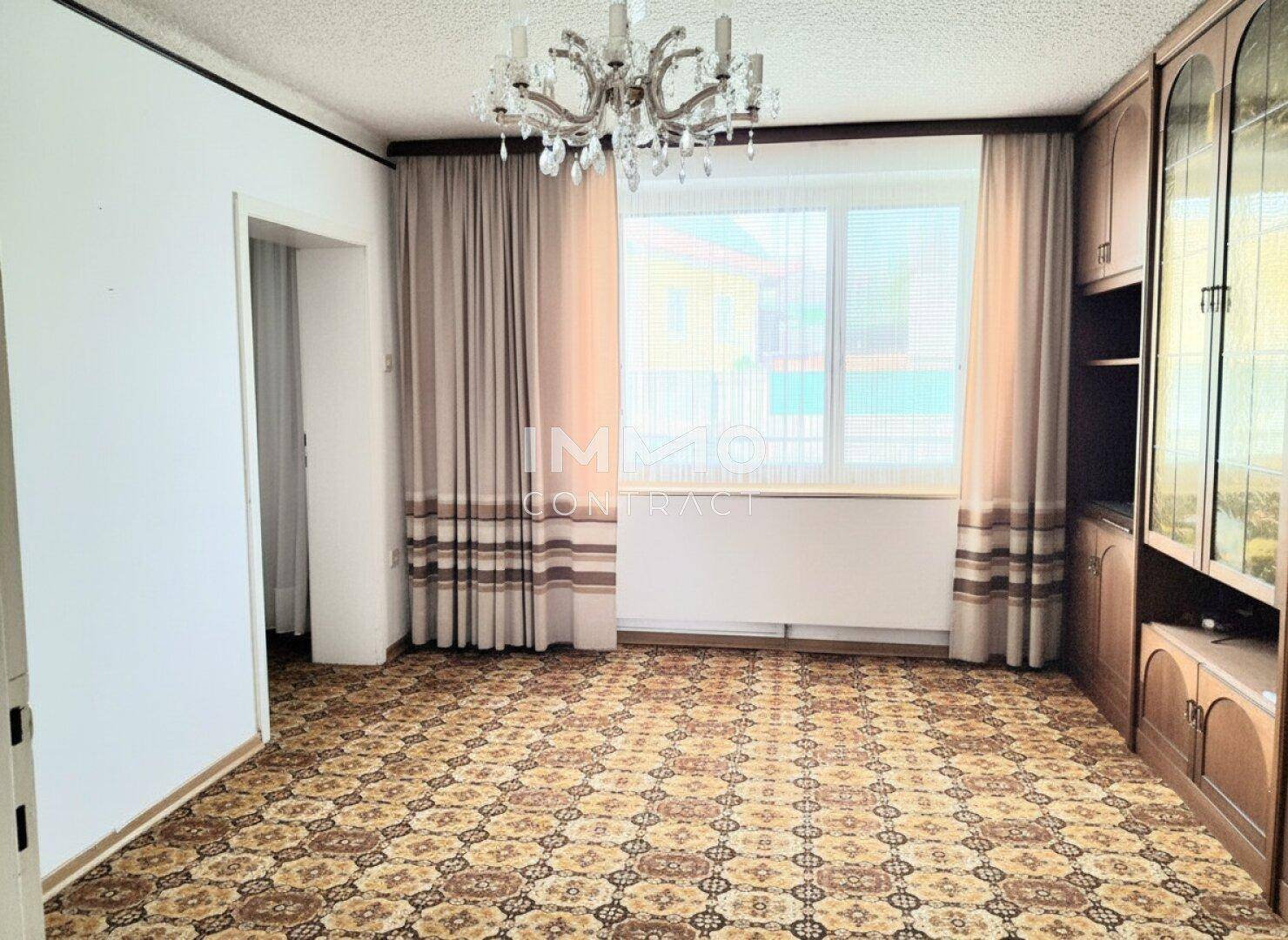 Geräumiges Wohnzimmer mit gemustertem Teppichboden und einem großen Fenster.