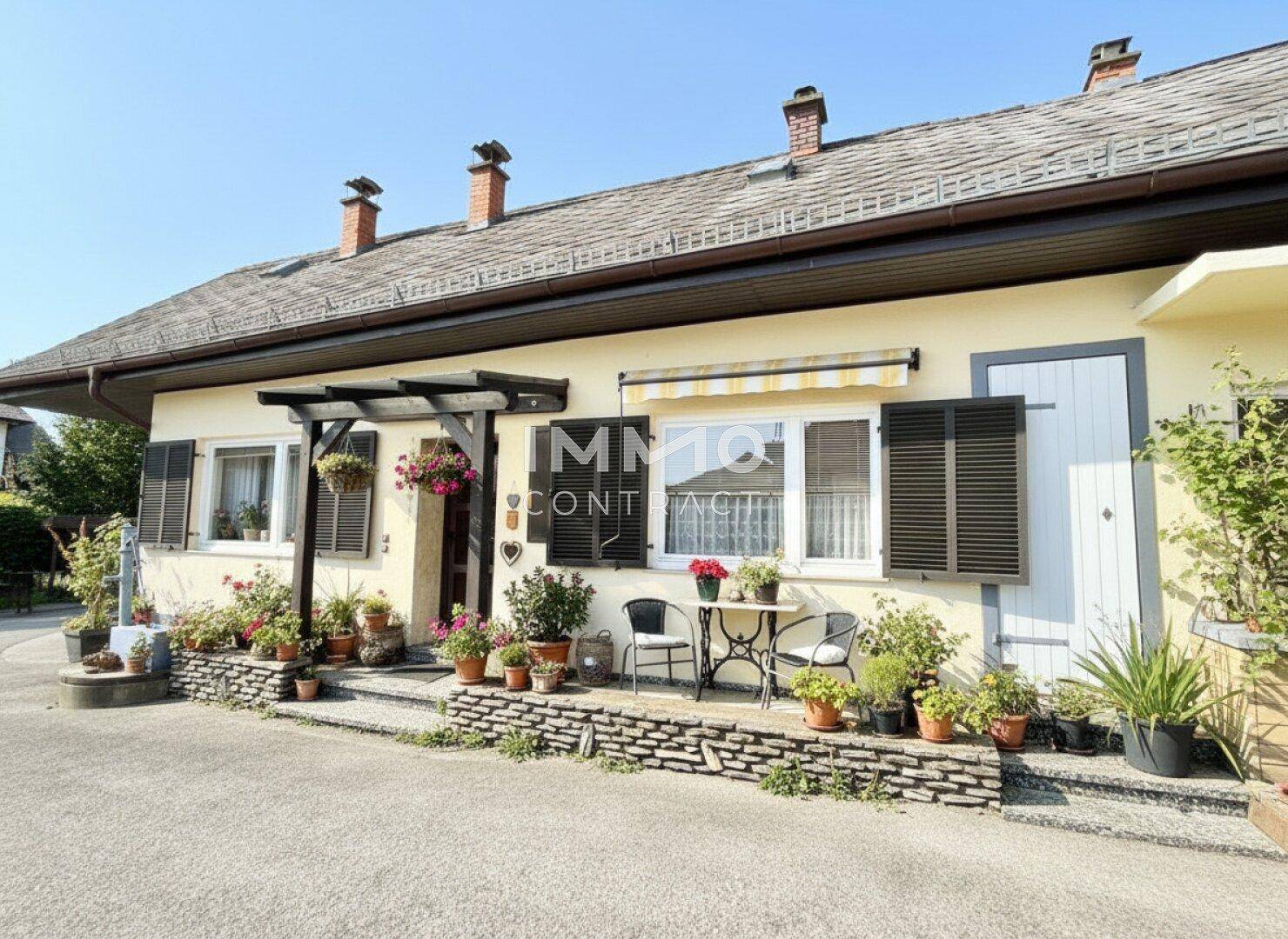 Hausfassade mit kleinen Fenstern, Fensterläden und einem gemütlichen Sitzbereich im Freien.