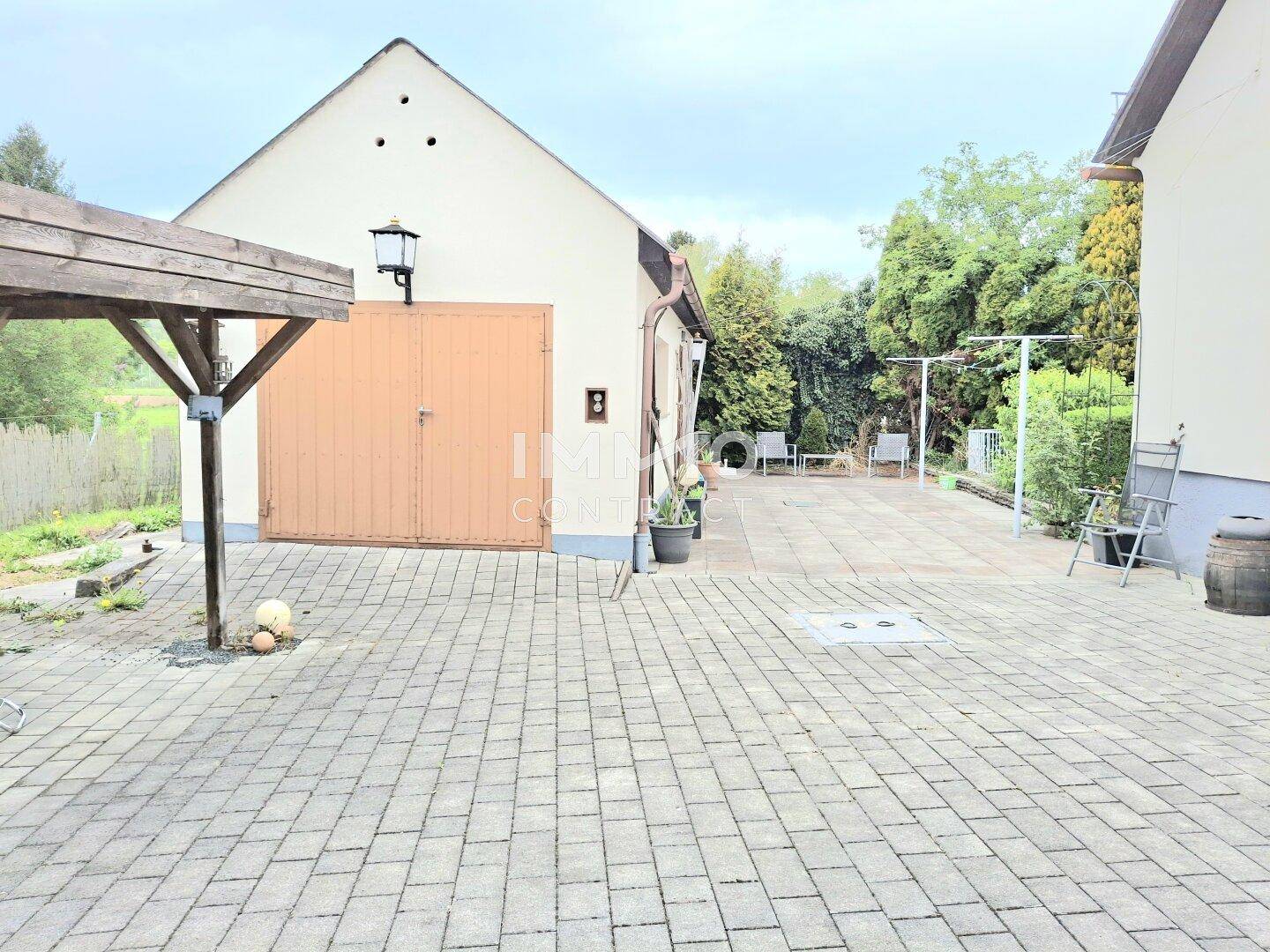 Gepflasterter Hofbereich mit Zugang zur Garage und einem überdachten Sitzplatz im Hintergrund.