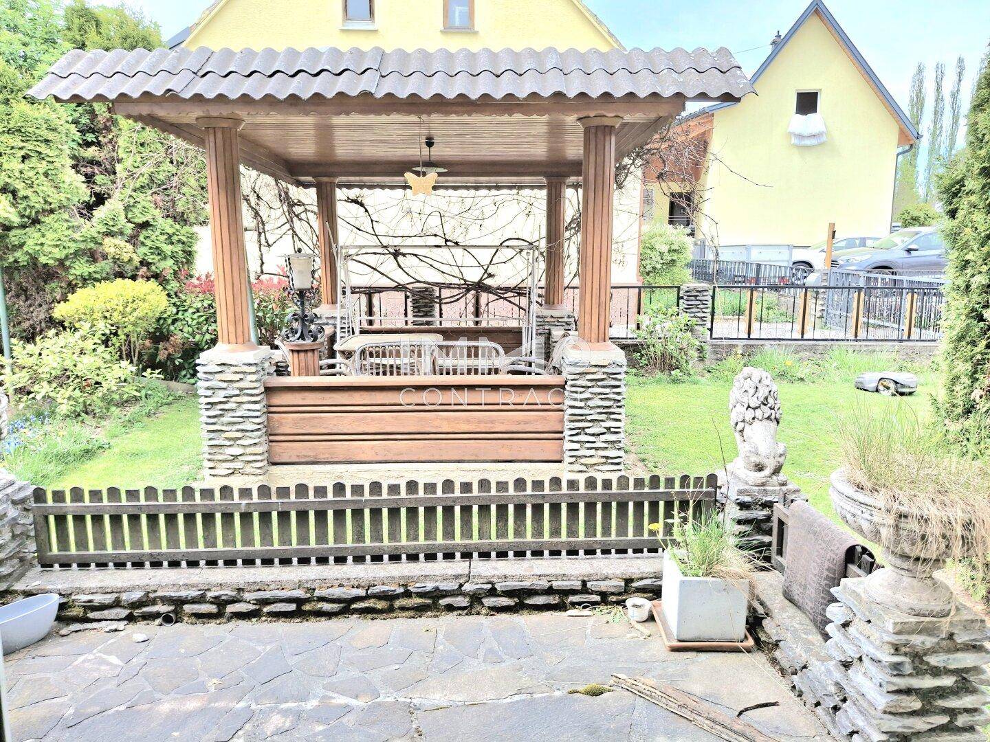 Idyllischer Garten mit einem dekorativen Pavillon und Steinfiguren.