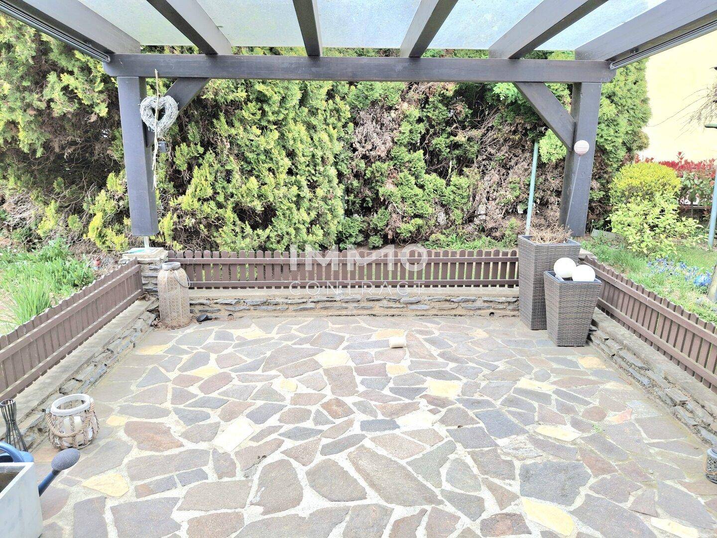 Große gepflasterte Terrasse unter einer Holzpergola, ideal für entspannte Stunden im Freien.