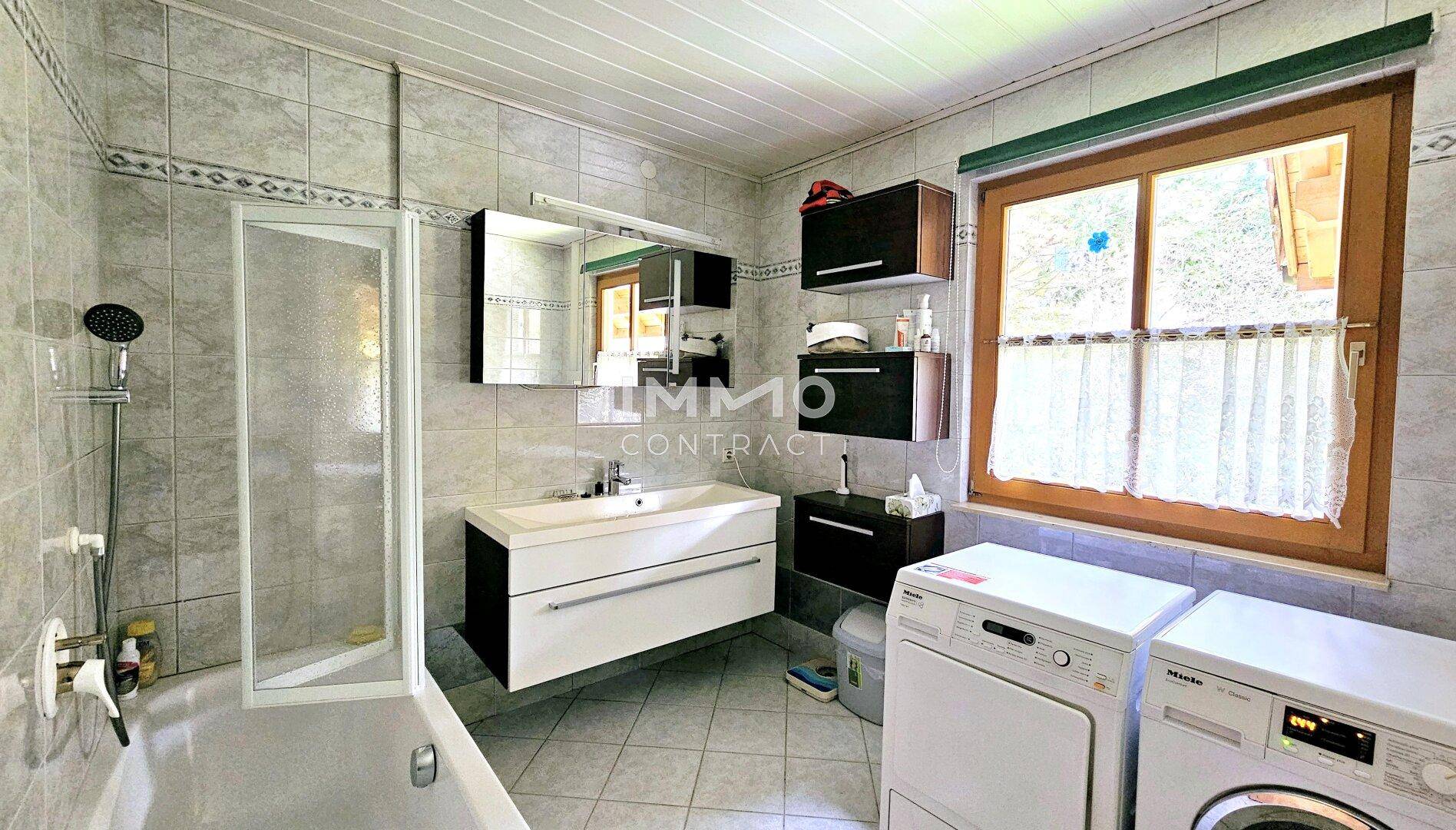 Gefliestes Badezimmer mit Badewanne, Dusche, Waschmaschine und Fenster.