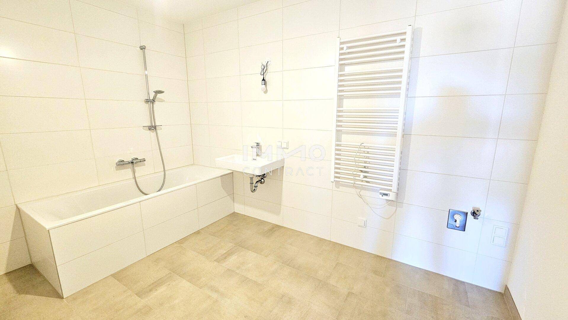 Modernes Badezimmer mit Badewanne, Handtuchheizkörper und hellen Fliesen an Wänden und Boden.