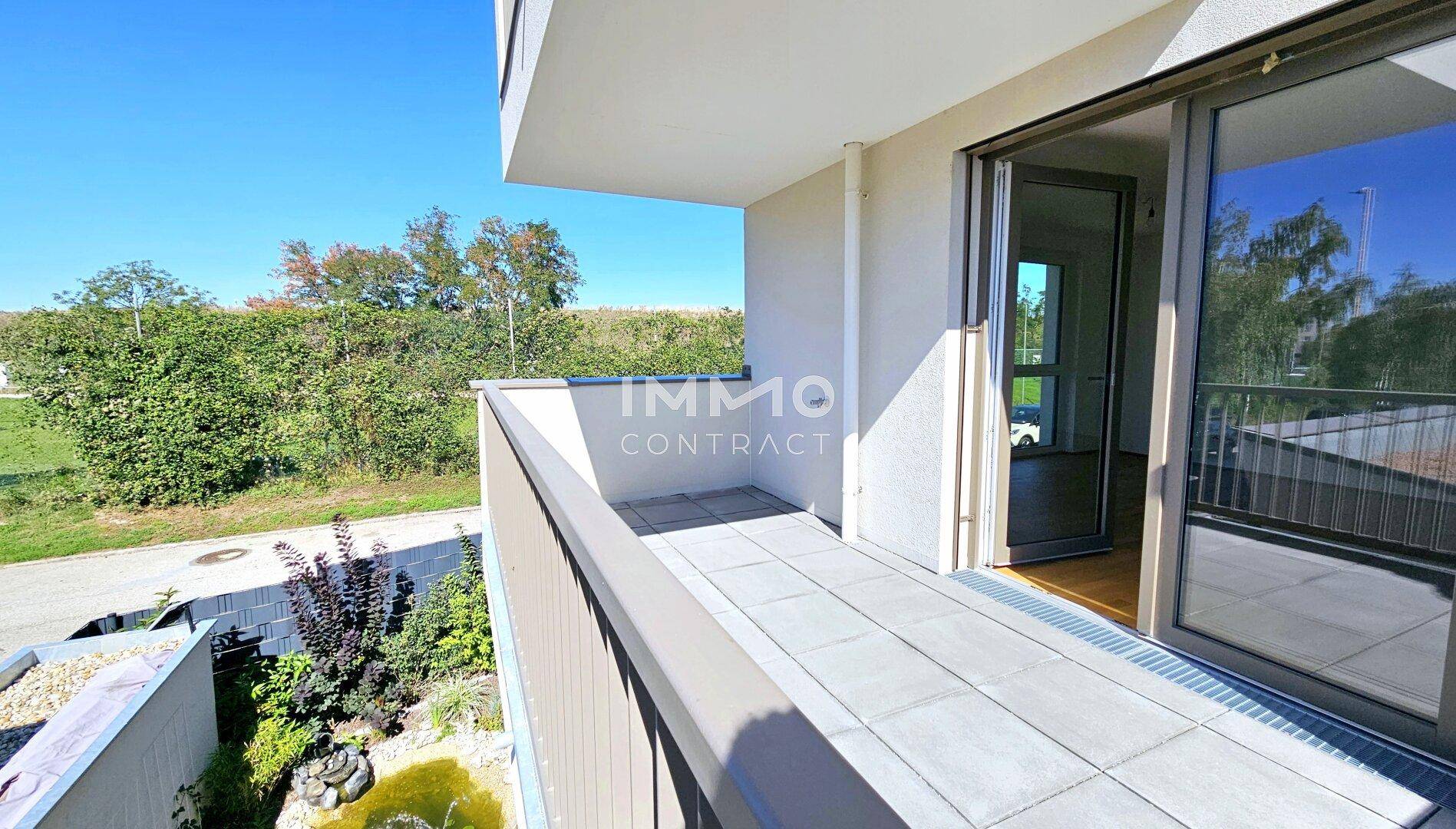 Sonniger Balkon mit Fliesenboden und Blick auf die grüne Umgebung und einen kleinen Teich.
