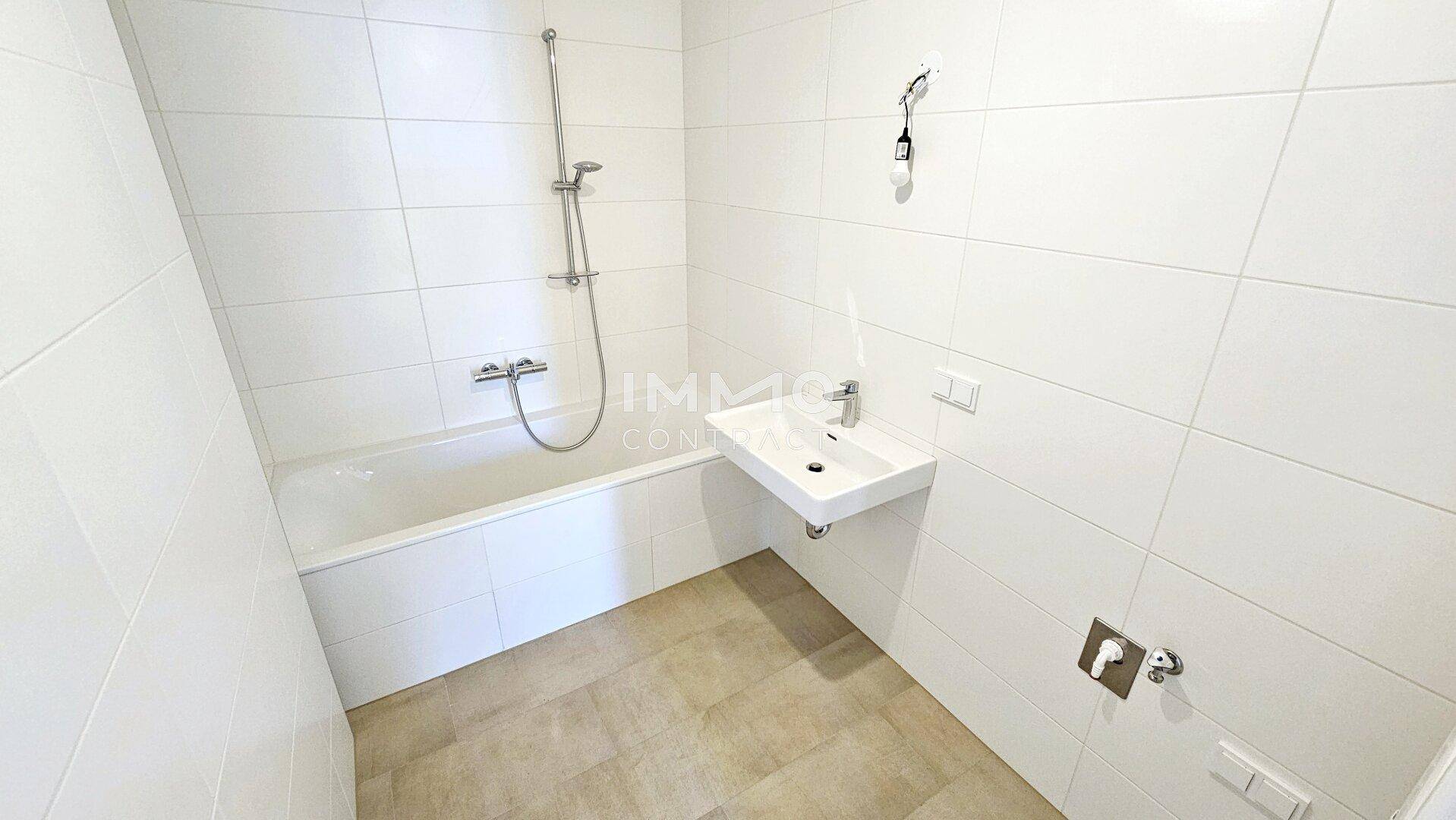 Modernes Badezimmer mit weißen Fliesen, Badewanne und wandhängendem Waschbecken.