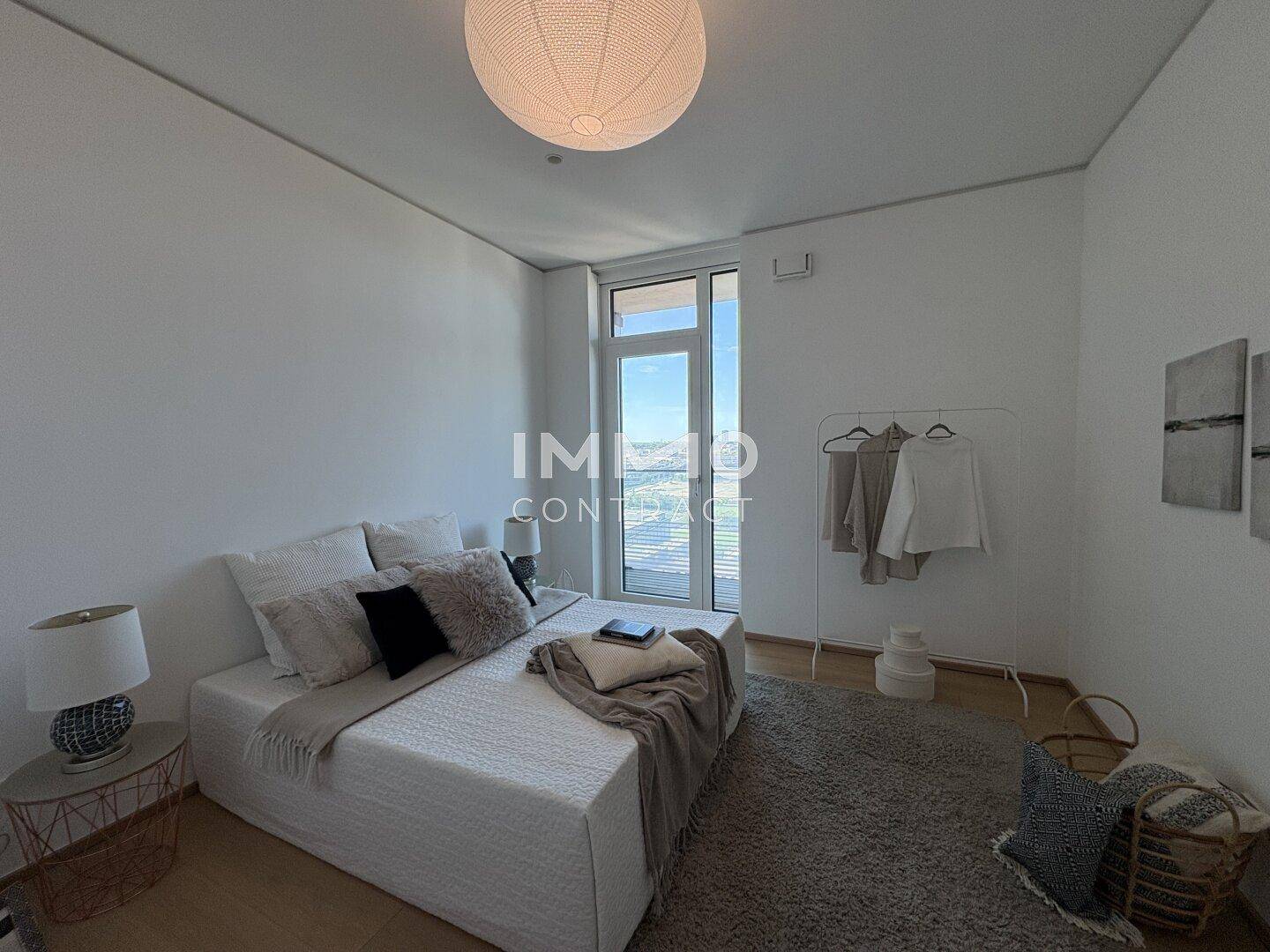 Modernes Schlafzimmer mit großem Bett, Teppichboden und Zugang zu einem Balkon.