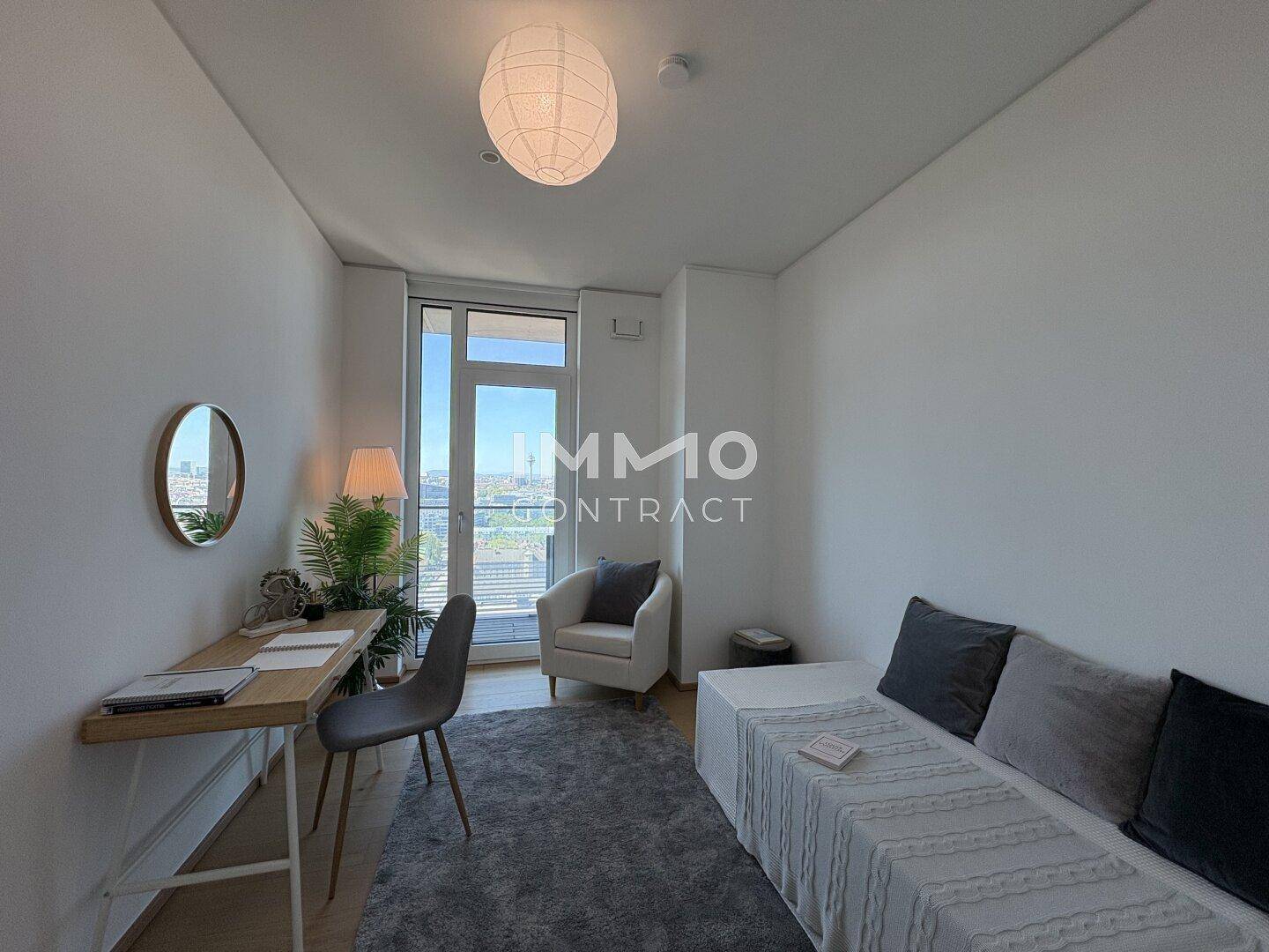 Helles Arbeitszimmer mit Schreibtisch, Tagesbett und großem Fenster mit Stadtblick.