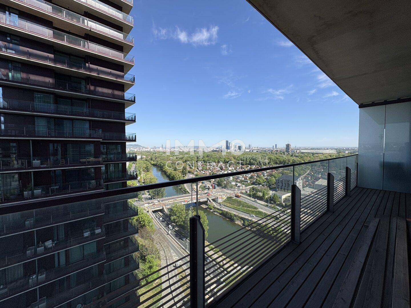 Großer Balkon mit Holzboden, Glasgeländer und Panoramablick auf Stadt und Fluss.