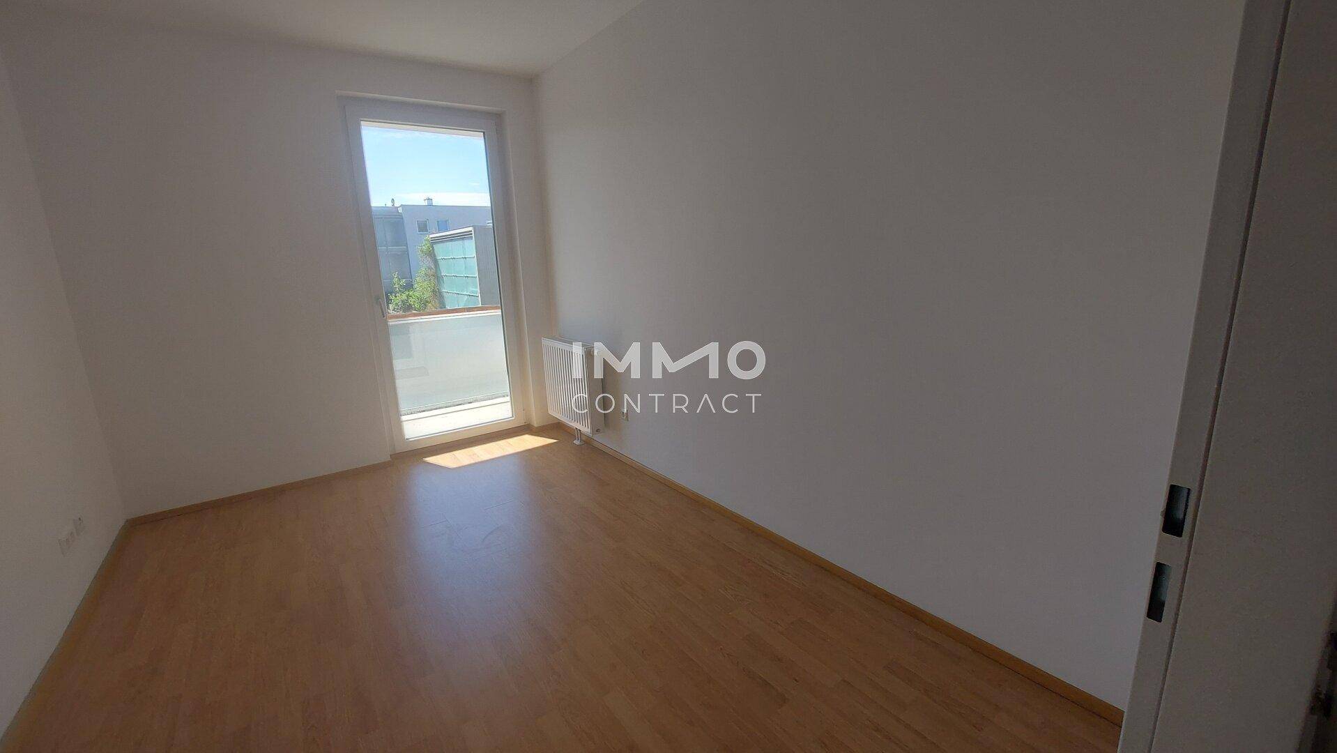 Helles Schlafzimmer mit Laminatboden und Fenster, das viel Tageslicht hereinlässt.