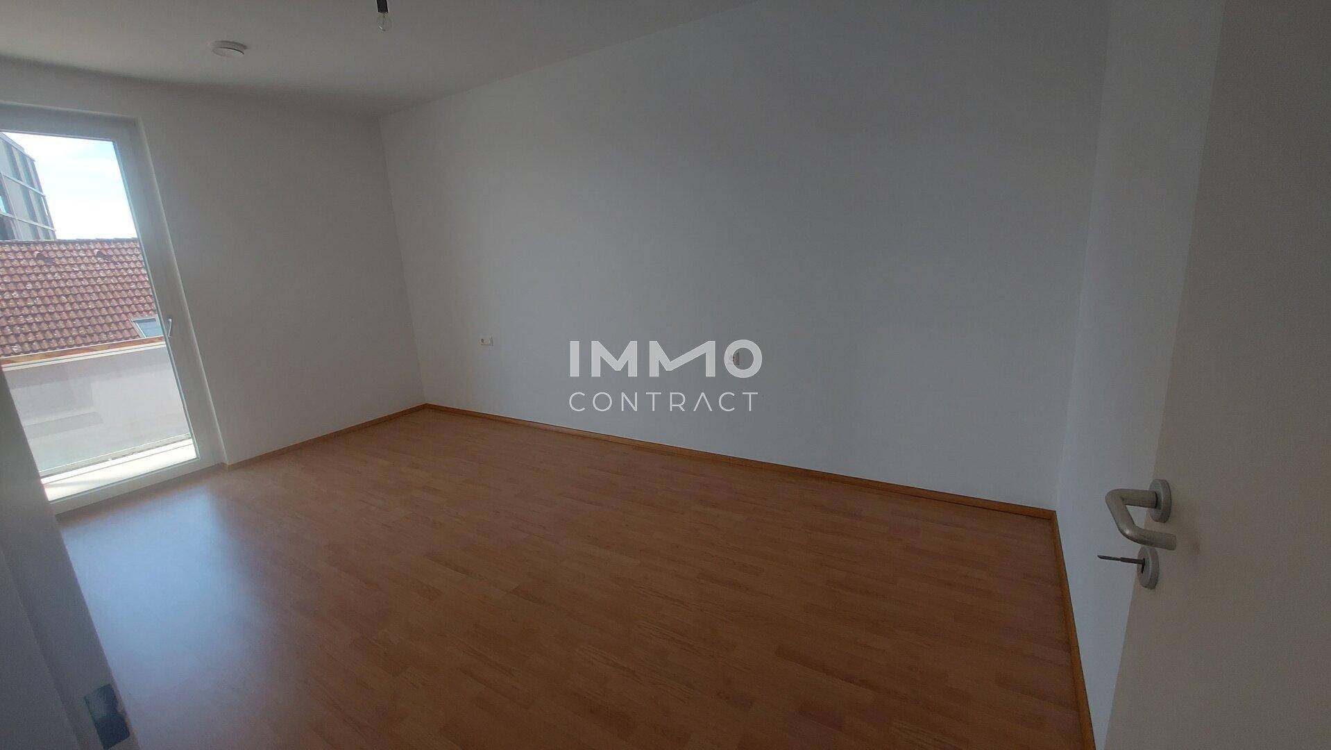 Leeres Schlafzimmer mit Laminatboden und Fenster, das viel Tageslicht hereinlässt.