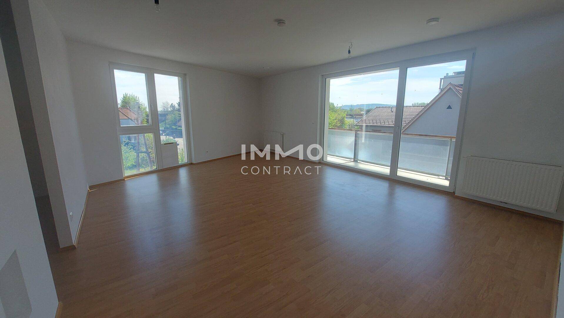 Heller Wohnraum mit großen Fenstern, Laminatboden und Zugang zum Balkon.