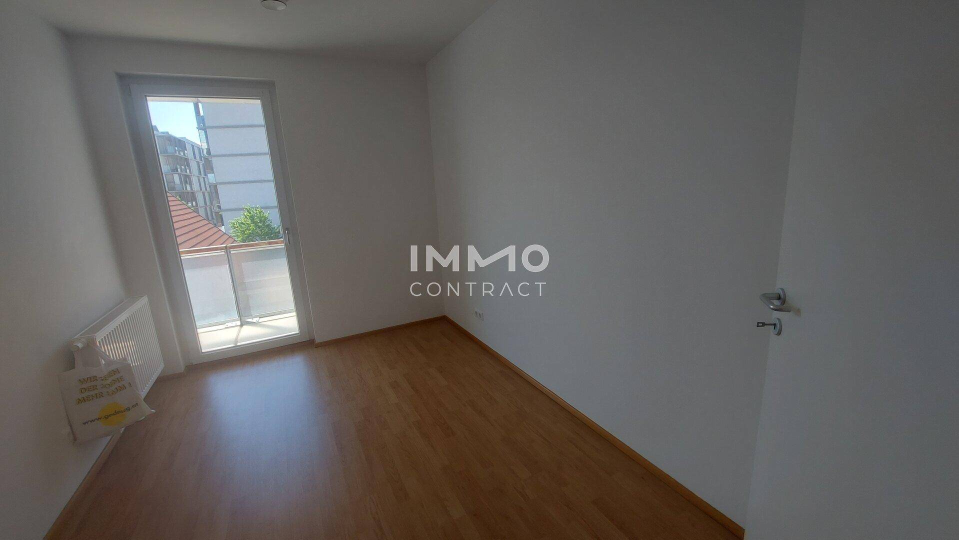 Helles Schlafzimmer mit Laminatboden, Heizkörper und Zugang zum Balkon.