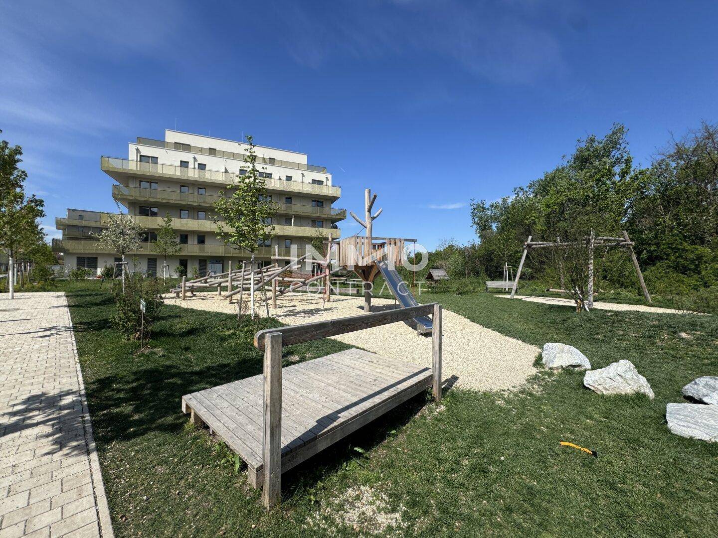 Modernes Wohngebäude mit einem Spielplatz im Vordergrund, umgeben von Grünflächen.