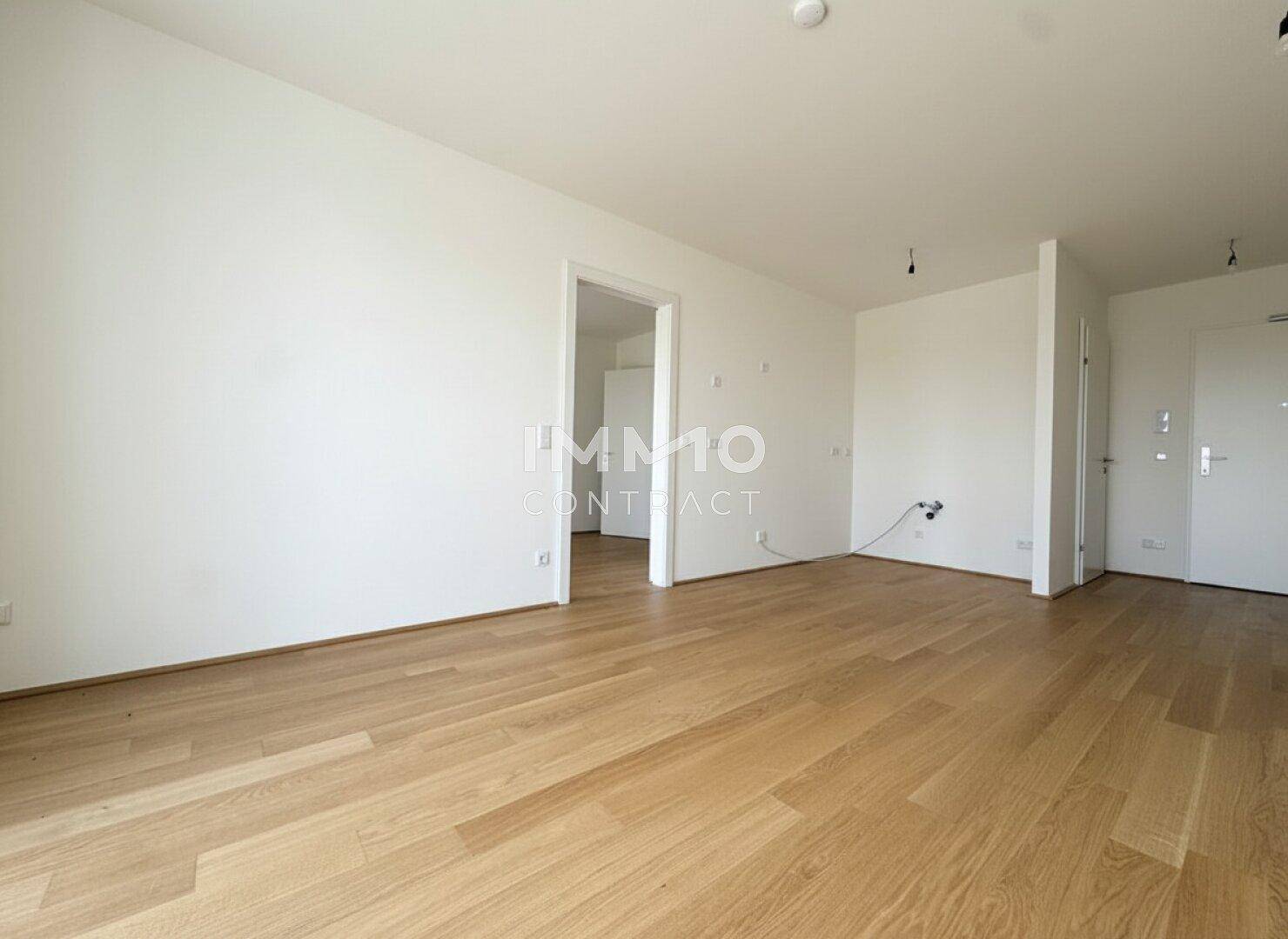 Geräumiges, unmöbliertes Zimmer mit hellem Holzboden und weiß gestrichenen Wänden.