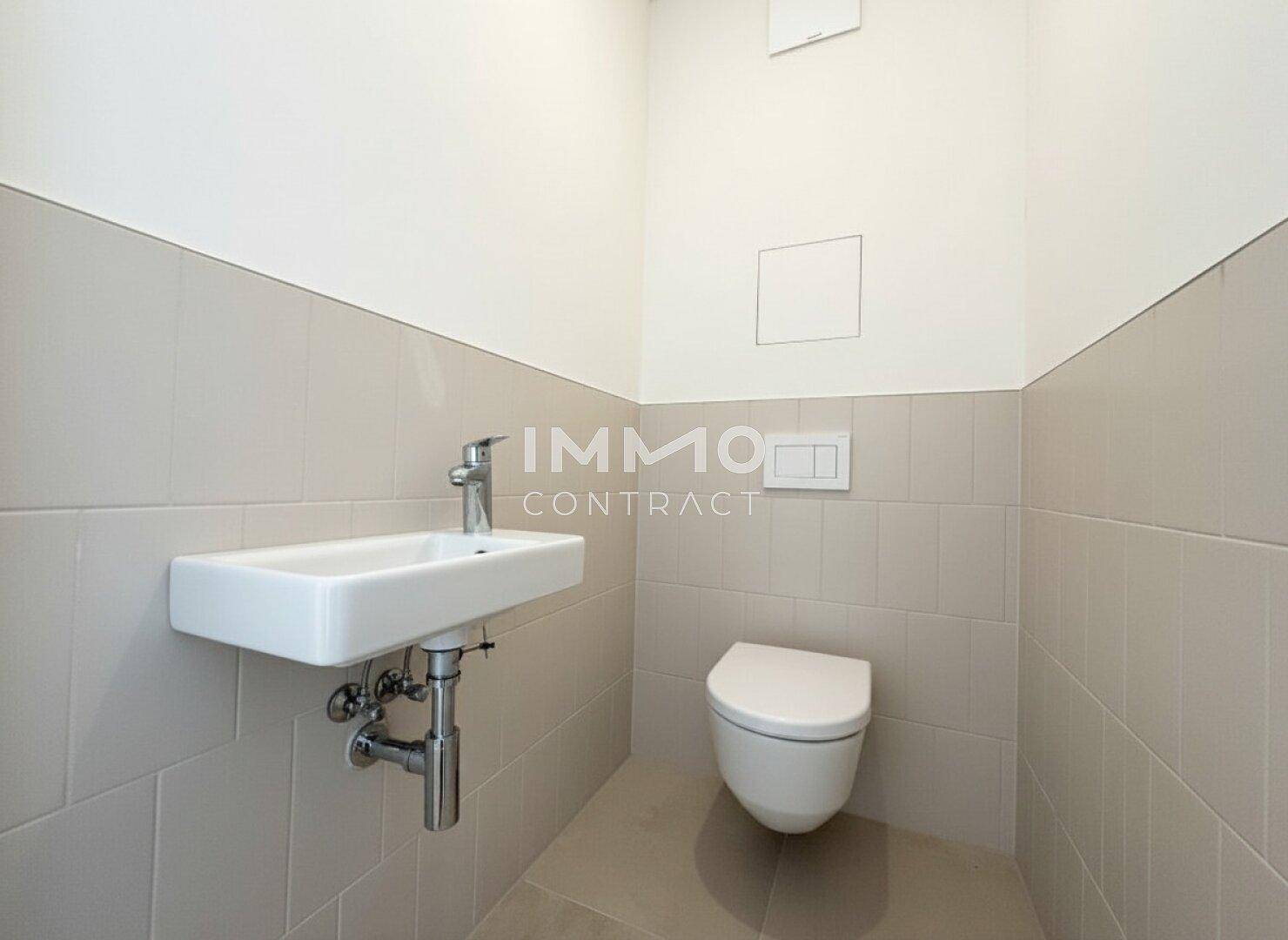 Separates Gäste-WC mit wandhängender Toilette und kleinem Waschbecken, hell gefliest.