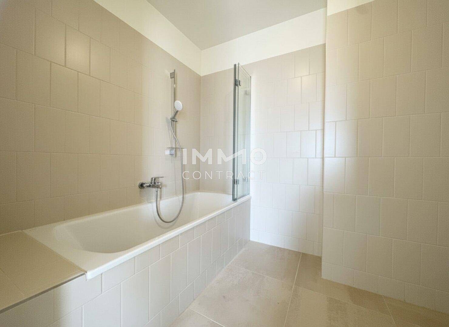 Modernes Badezimmer mit Badewanne und Duschvorrichtung, komplett gefliest in hellen Farbtönen.