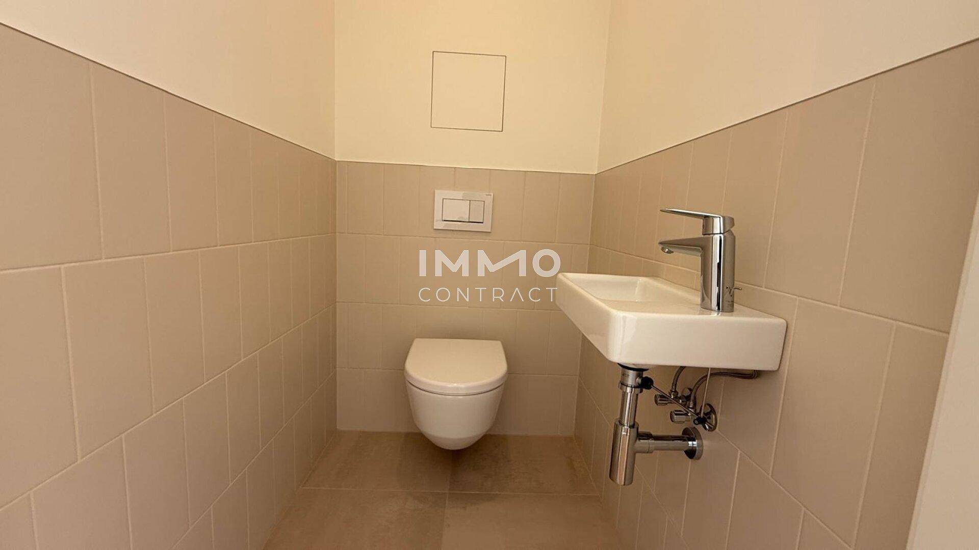 Modernes Gäste-WC mit Wand-WC und kleinem Waschbecken, hell gefliest.