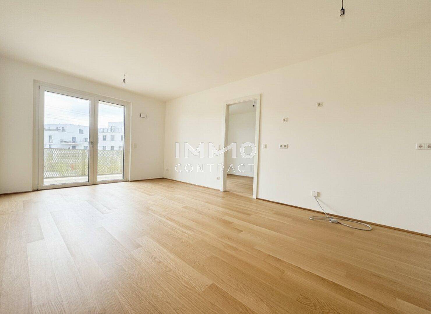 Geräumiger, unmöblierter Raum mit Holzboden und großen Fenstern zum Balkon.