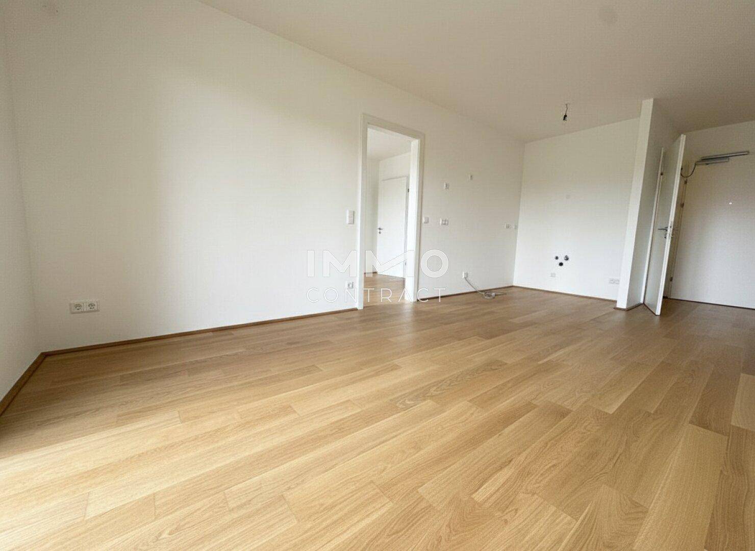 Heller, unmöblierter Wohnbereich mit Holzboden und Zugang zu weiteren Räumen.