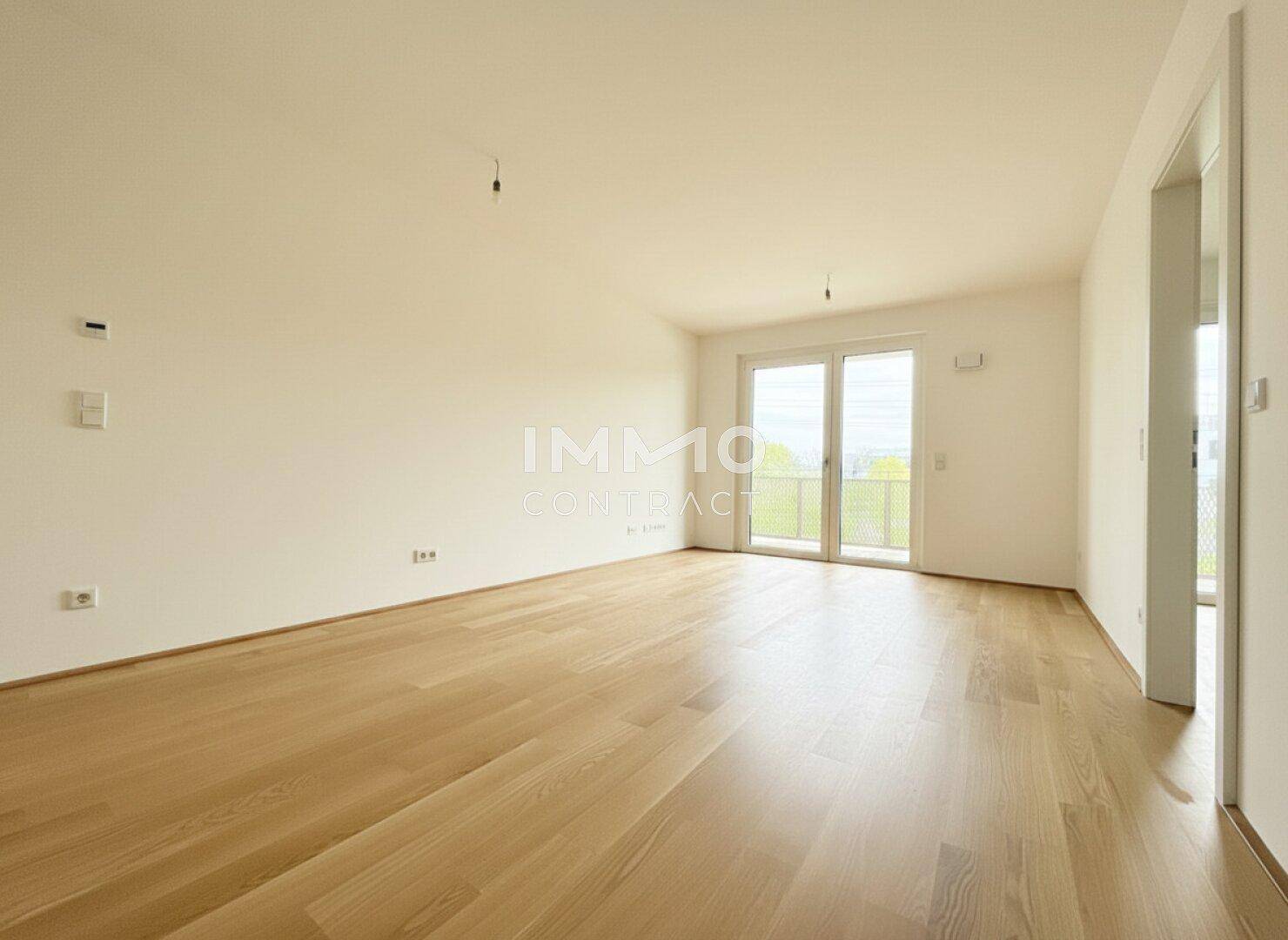 Heller, leerer Raum mit Holzboden und viel Tageslicht durch die Balkontür.