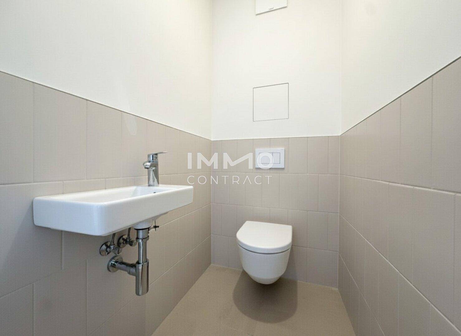 Gäste-WC mit wandhängendem WC, kleinem Waschbecken und hellen Fliesen.
