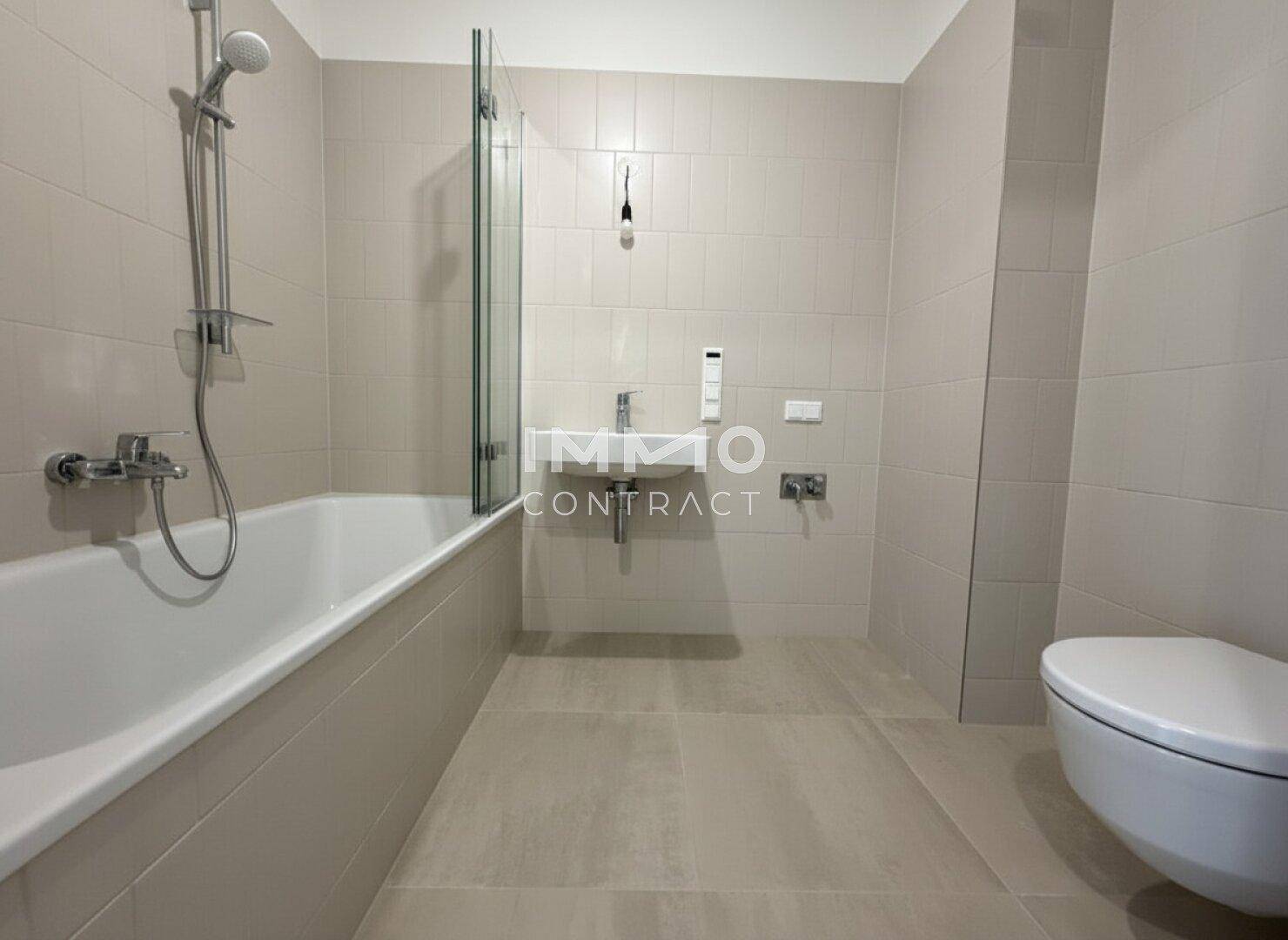 Modernes Badezimmer mit hellen Fliesen, Badewanne mit Duschfunktion, Waschbecken und wandhängendem WC.
