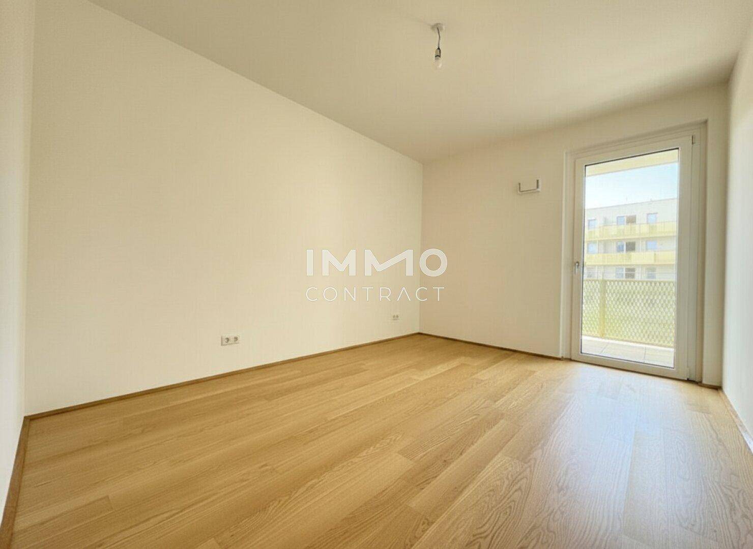 Ruhiges, unmöbliertes Schlafzimmer mit hellem Parkettboden und direktem Zugang zu einem Balkon.