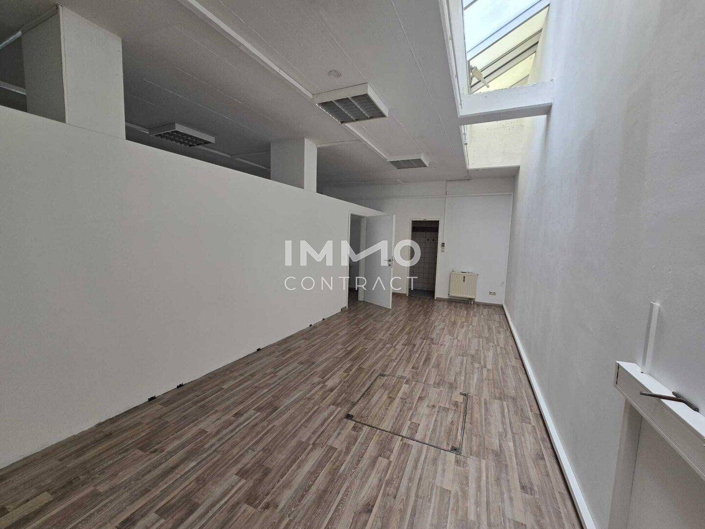 Langer Bürobereich mit Holzboden, weißen Wänden und einem großen Oberlicht für viel Helligkeit.